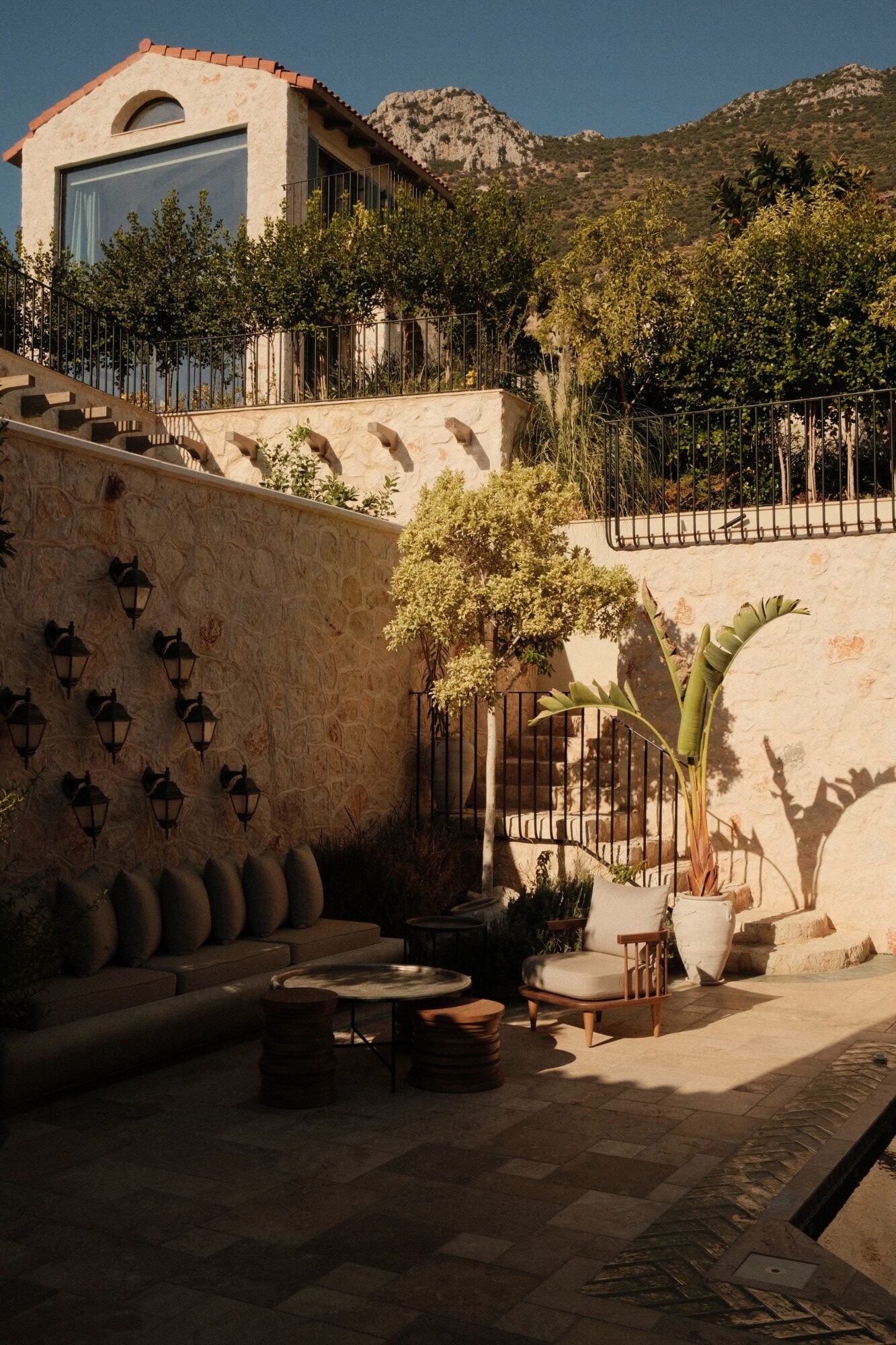 Villa Thalia by Muses Kalkan, Kalkan, Turkey — Courtyard with stone terraces, black lanterns, cushioned seating, potted plants, and mountain vista at golden hour.