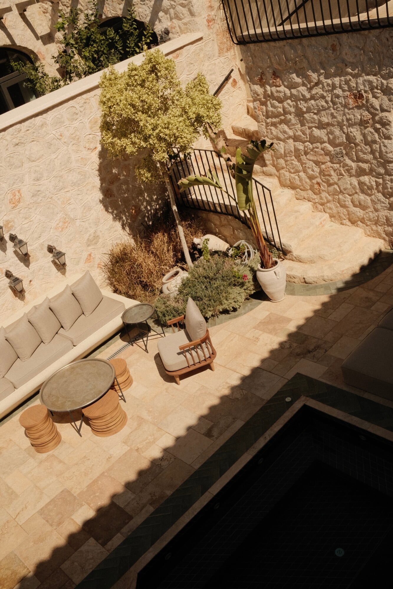 Villa Thalia by Muses Kalkan, Kalkan, Turkey — Aerial view of limestone courtyard with contemporary seating, potted plants, and climbing vines casting shadows on stone walls.