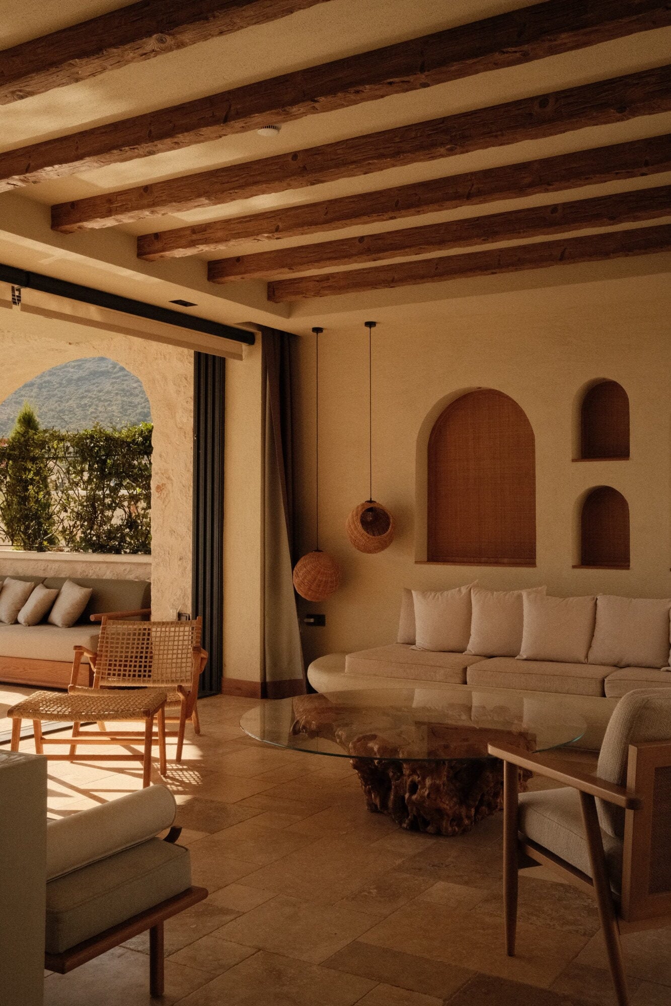 Villa Thalia by Muses Kalkan, Kalkan, Turkey — Minimalist living room with exposed wooden beams, arched doorways, cream linen seating, and natural stone coffee table overlooking terrace.