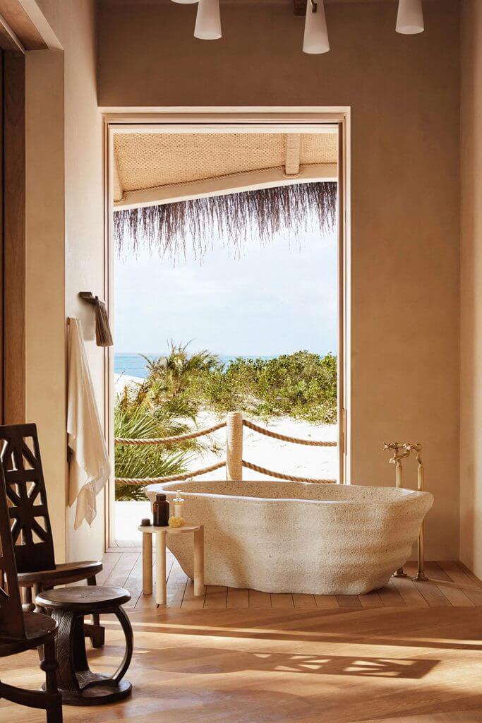 Kisawa Sanctuary, Africa — Coastal bathroom with stone soaking tub, thatch-roof pavilion, ocean view, natural materials, and minimalist tropical design.