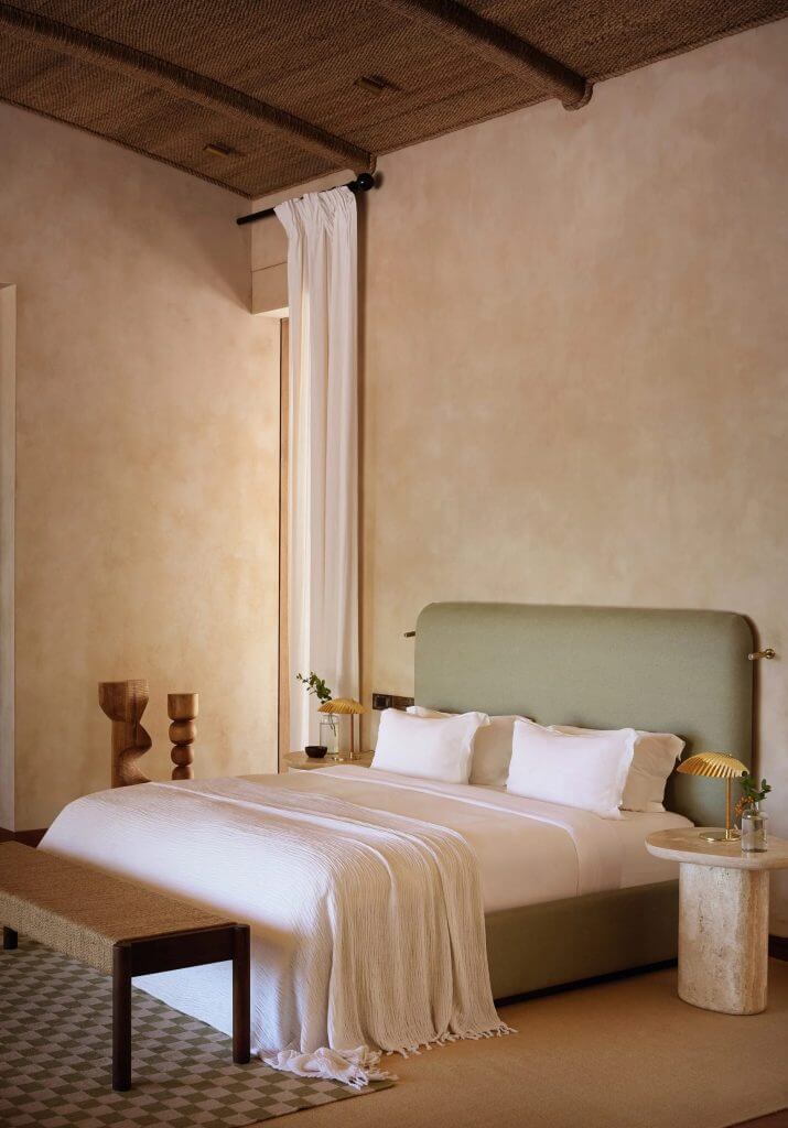 Kisawa Sanctuary, Africa — Minimalist bedroom with sage green headboard, woven ceiling detail, cream linen bedding, and natural light from floor-to-ceiling curtains.