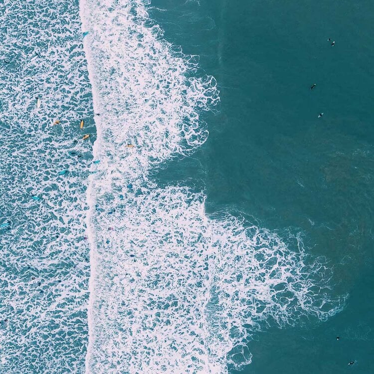 Abodu x Koto, North America — Aerial view of turquoise ocean waves breaking on sandy beach at sunset, minimalist coastal landscape.