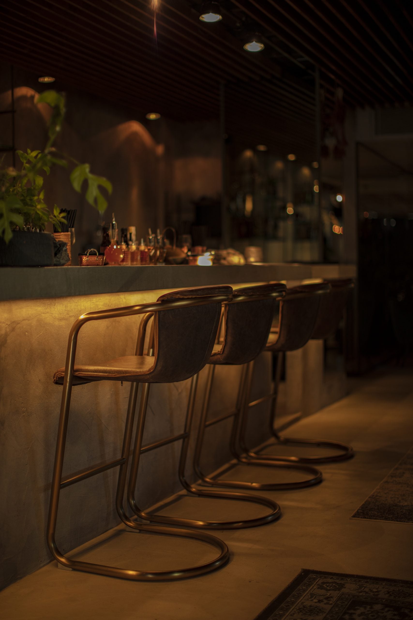 Laylah, Balearic Islands — Minimalist bar counter with brass cantilever stools, warm ambient lighting, and sleek modern interior design.