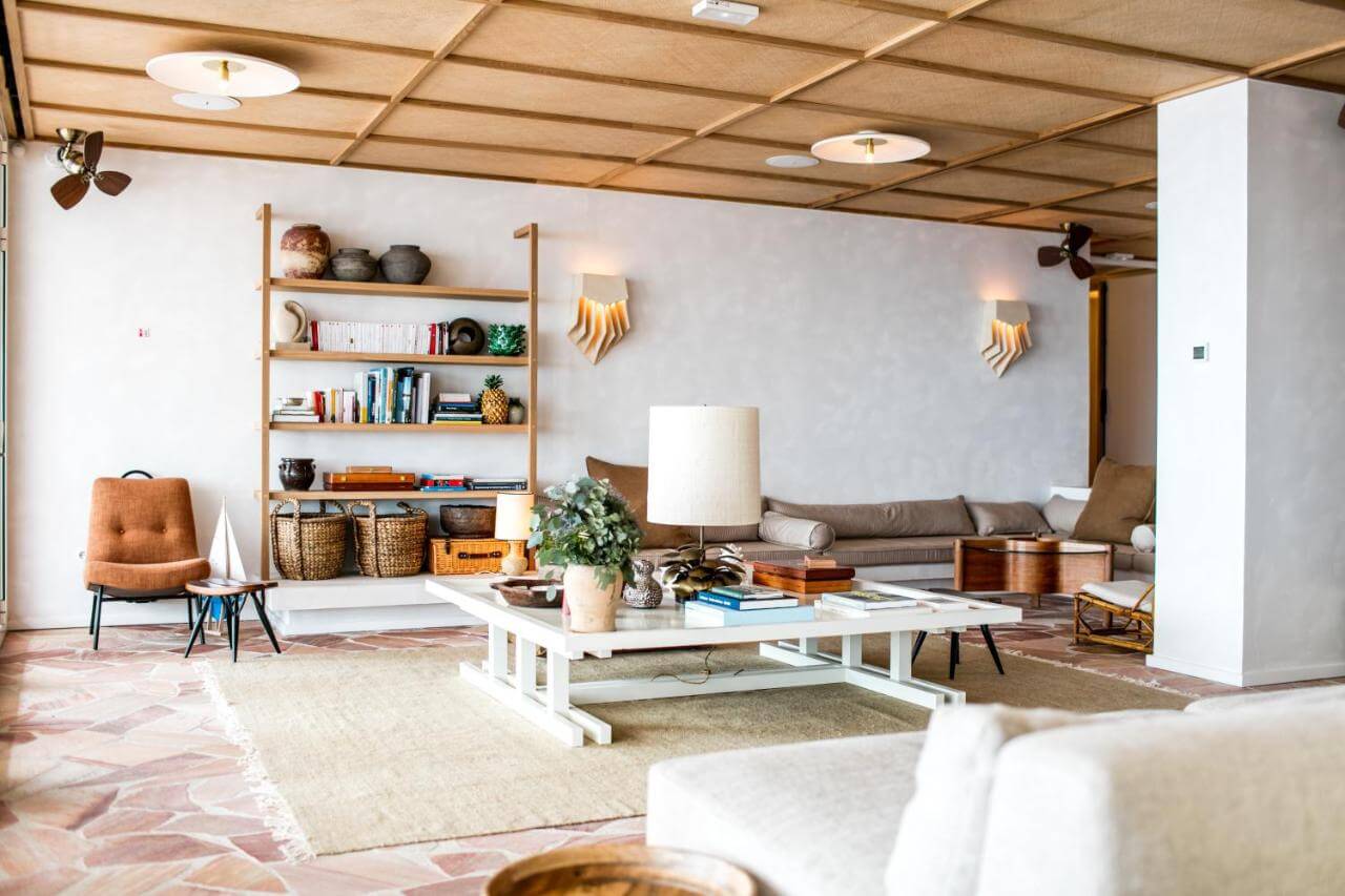 Les Roches Rouges, Europe — Mid-century modern living room with wooden ceiling, leather chair, wall-mounted shelving, white coffee table, and layered natural lighting.