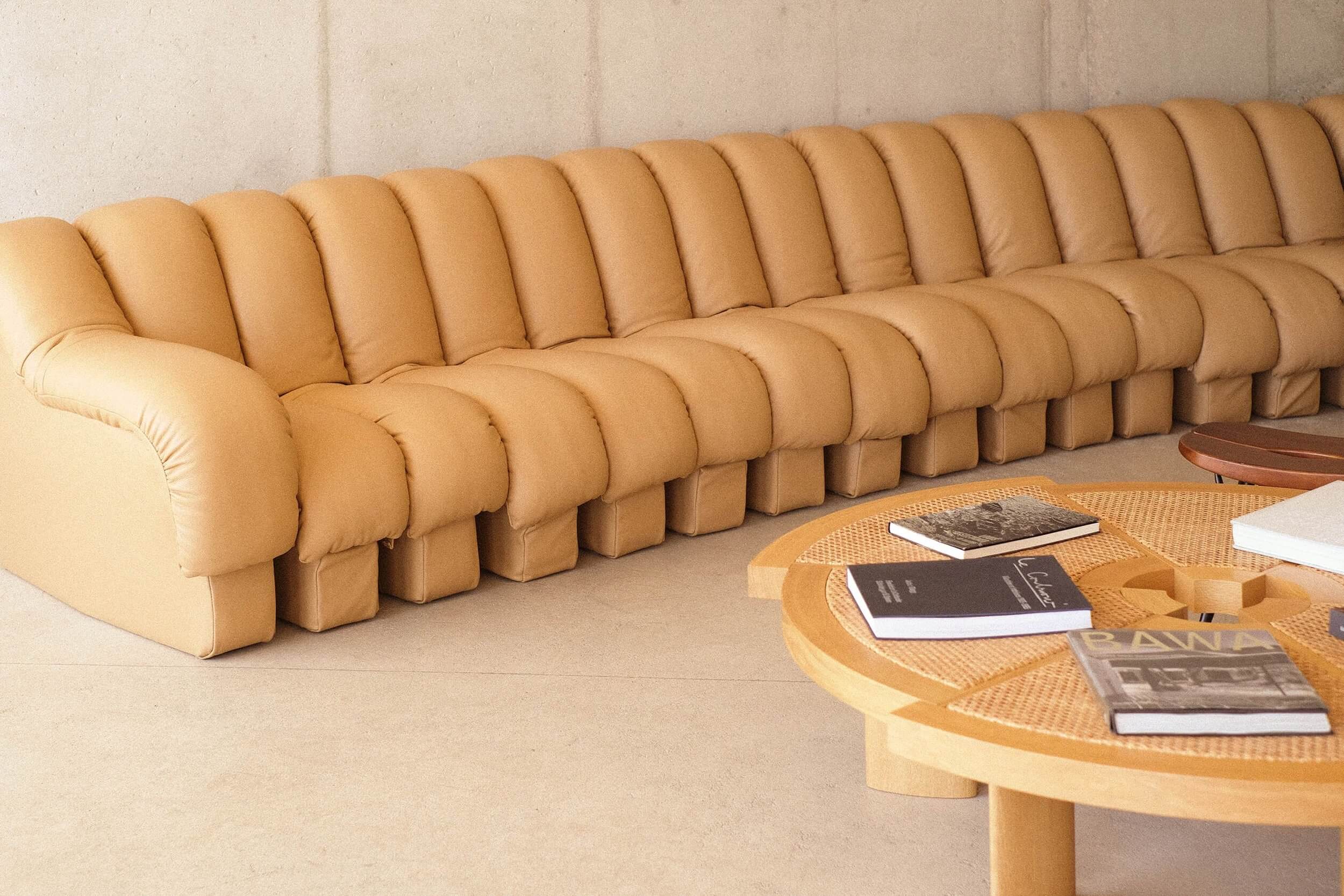 Les Roches Rouges, Europe — Caramel leather modular sofa with ribbed cushioned segments, wooden side table with woven surface, minimalist hospitality interior design.