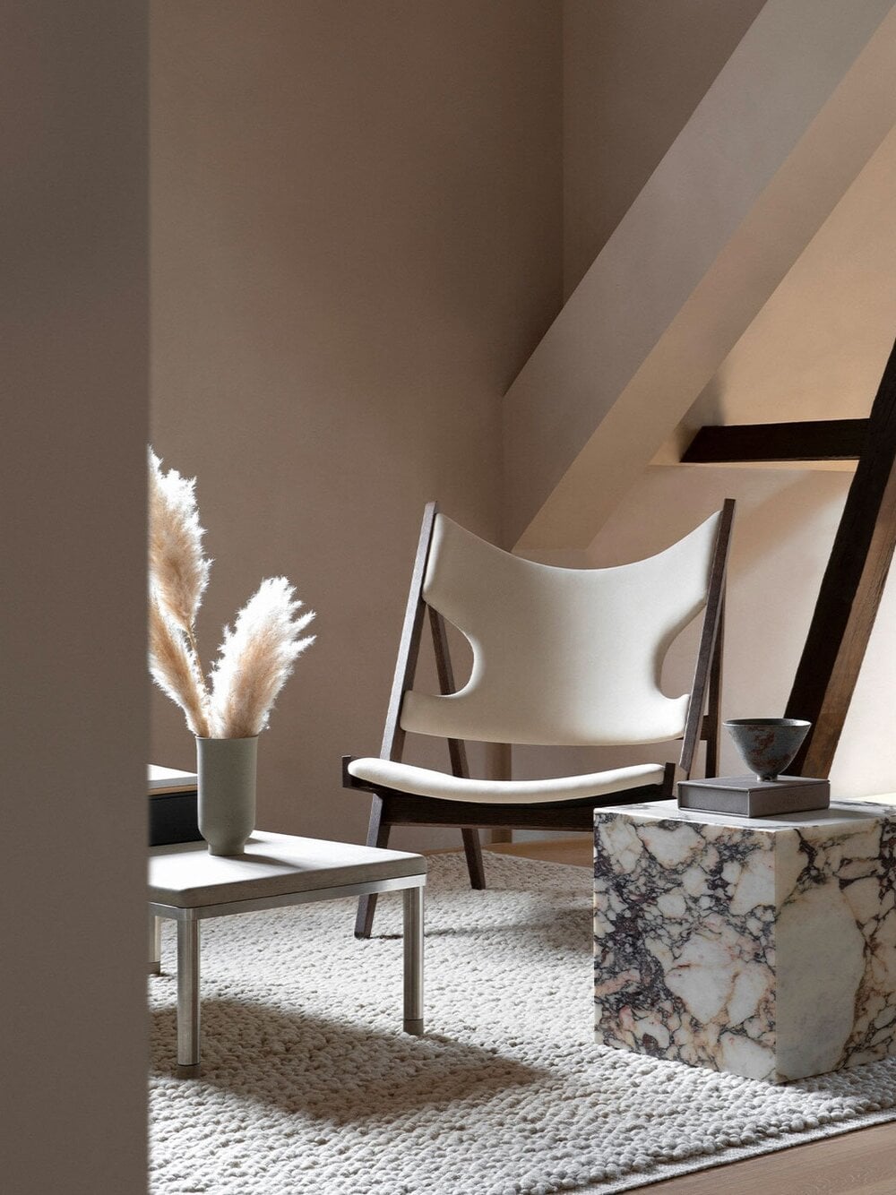 The Audo, Europe — Minimalist lounge with cream curved chair, marble side table, pampas grass in ceramic vase, natural light, neutral palette, contemporary design.