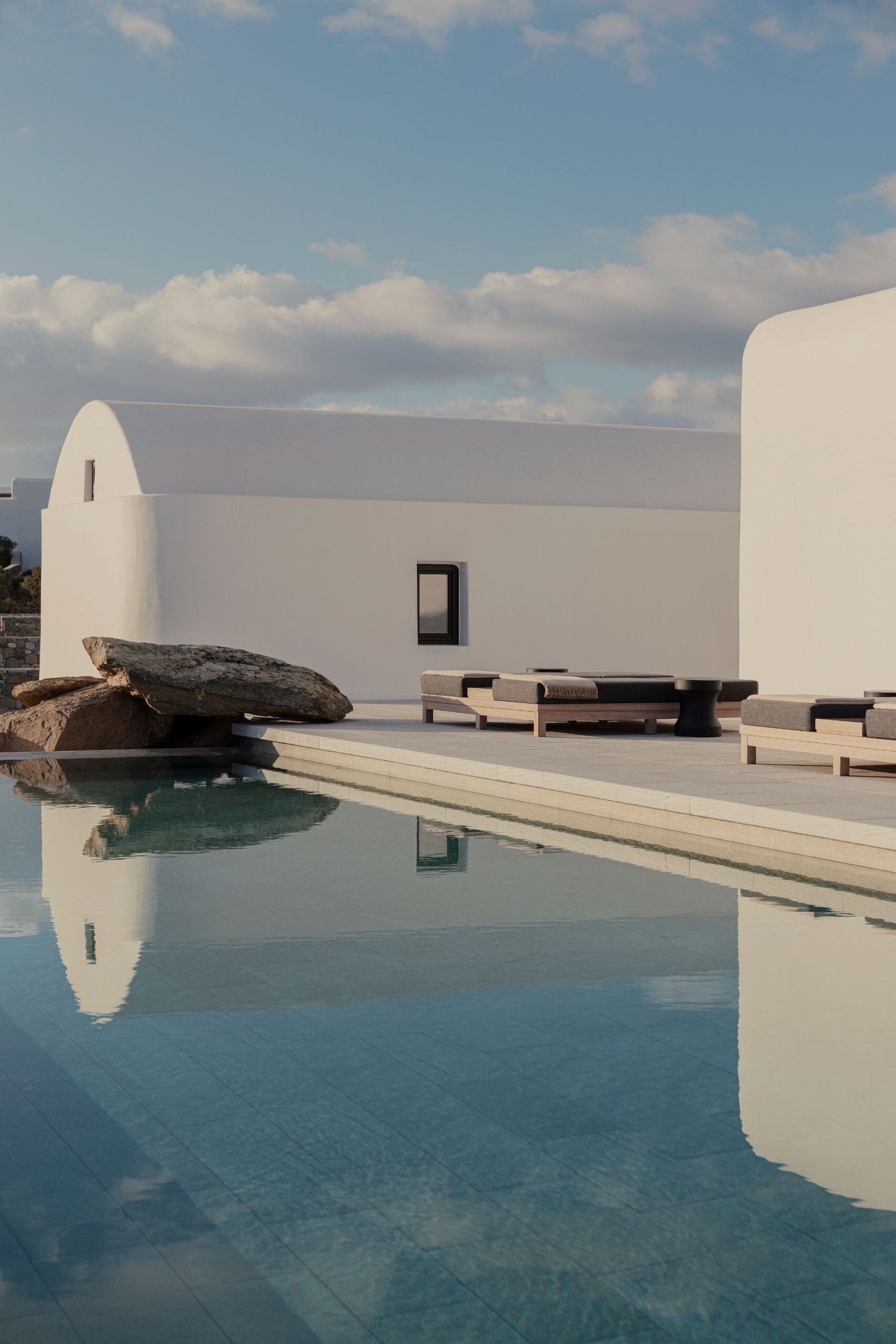 Kalesma Hotel, Europe — Minimalist white architecture with curved walls, infinity pool reflecting sky, natural stone, wooden loungers, Mediterranean coastal design.