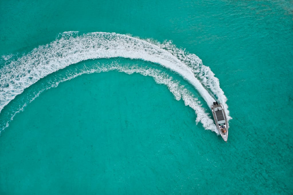 Private Boat and Fishing Charters — Luxury speedboat cutting through turquoise tropical waters, aerial view of white wake pattern and pristine ocean destination.