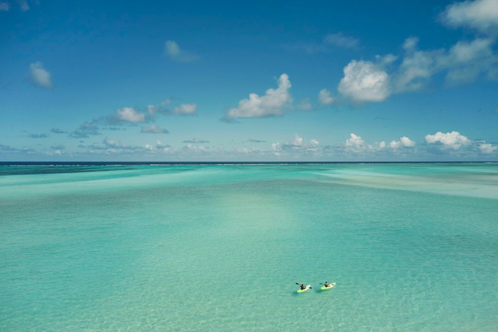 COMO Parrot Cay, North America — Two kayakers in crystalline turquoise lagoon beneath blue sky with white clouds, tropical atoll seascape.