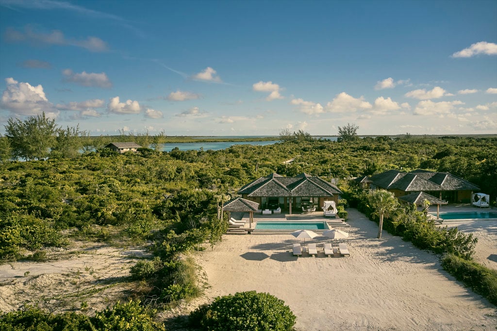 COMO Parrot Cay, Turks and Caicos — Modernist beachfront villa with infinity pool overlooking mangrove lagoon and turquoise waters under clear sky.