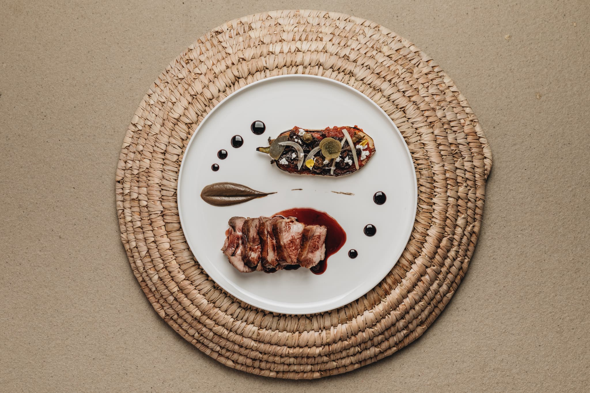 Parīlio Hotel, Europe — Plated fine dining dish with sliced duck breast, caramelized root vegetable, and microgreens on white ceramic against woven natural placemat.