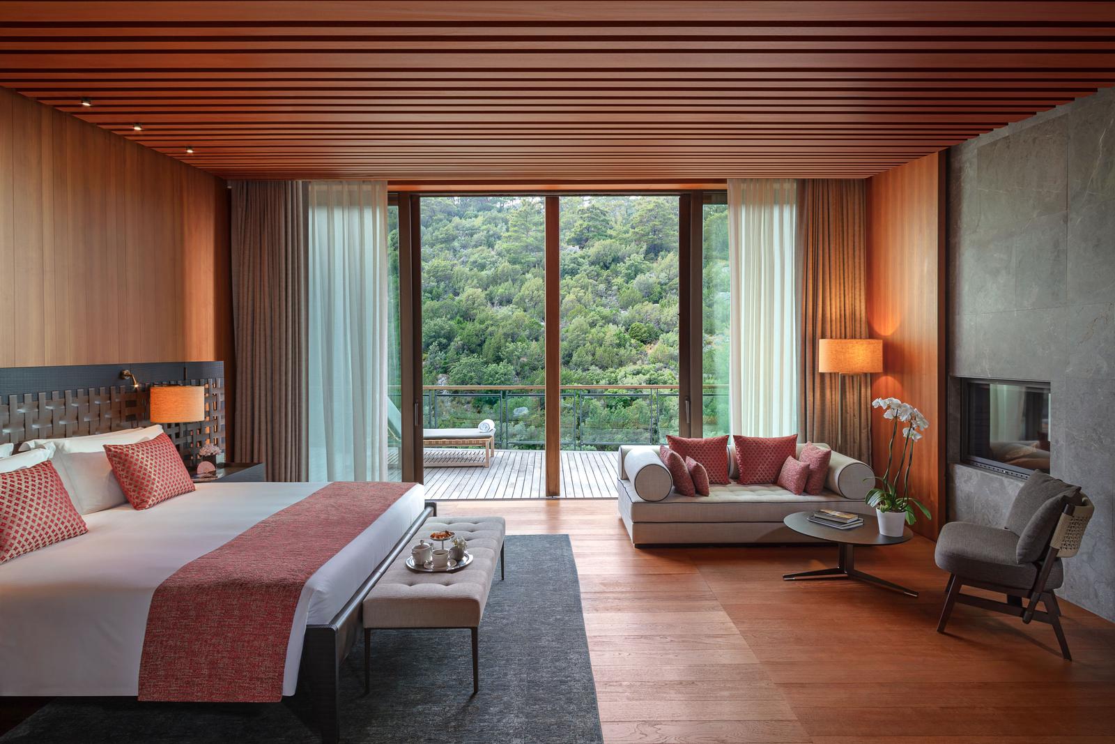 Mandarin Oriental Bodrum, Turkey — Modern luxury suite with wood ceiling, terracotta textiles, forest views through floor-to-ceiling windows, and contemporary furnishings.