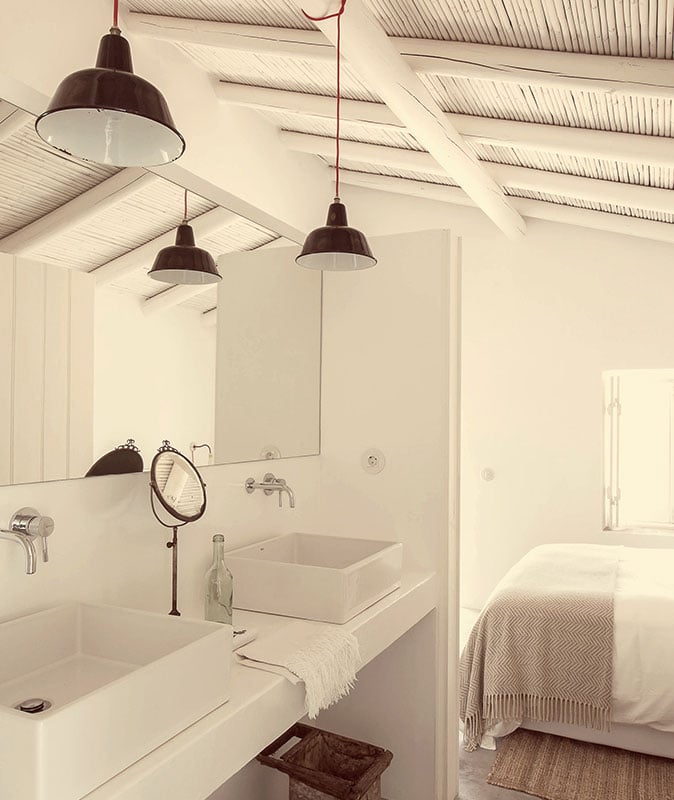 Pensão Agrícola, Europe — Minimalist ensuite bathroom with industrial pendant lights, white vessel sink, exposed beam ceiling, and adjacent bedroom with neutral linens.