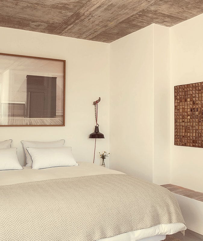 Pensão Agrícola, Europe — Minimalist bedroom with wooden ceiling, cream walls, linen bedding, vintage pendant lamp, and framed mirror reflecting architectural details.