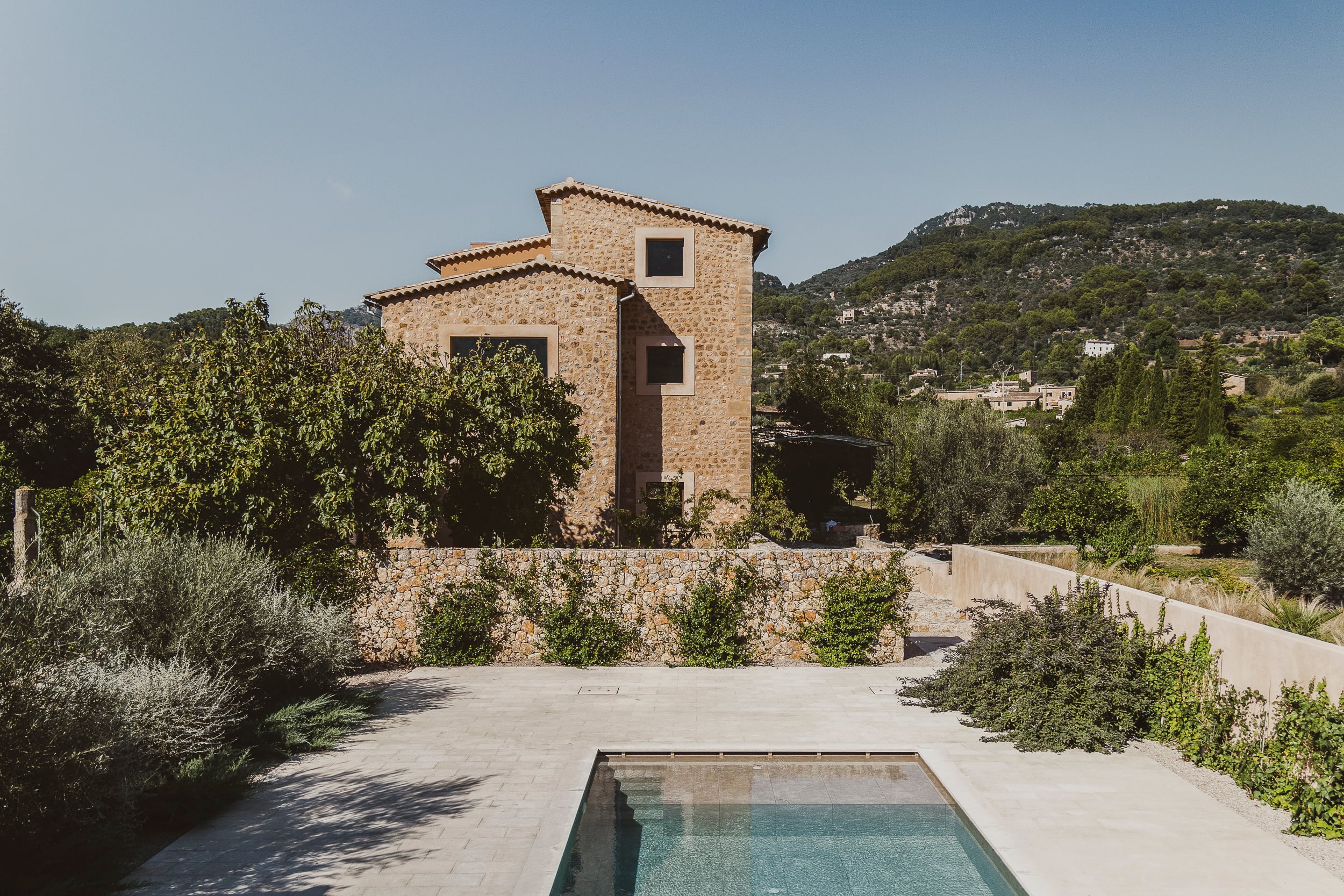 Can Gaspar, Balearic Islands, Spain — Stone tower with geometric windows overlooking terraced courtyard, olive trees, and forested Mediterranean hillside.