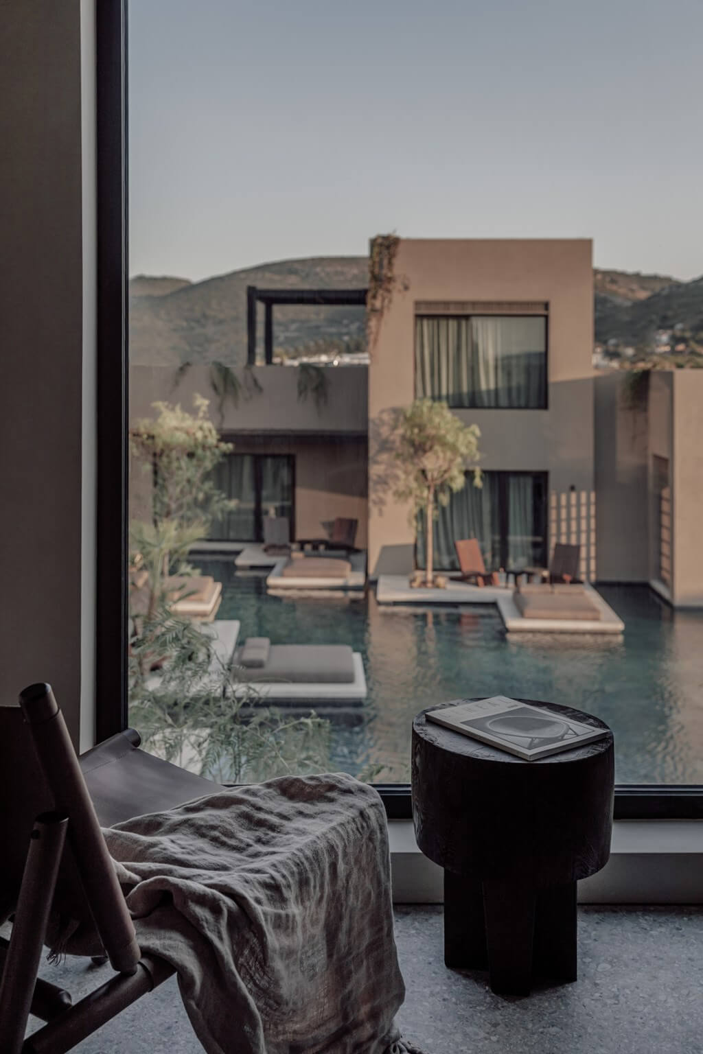 Casa Cook Samos, Greece — Modern bedroom with terrace overlooking infinity pool, minimalist furnishings, and hillside views in warm Mediterranean light.