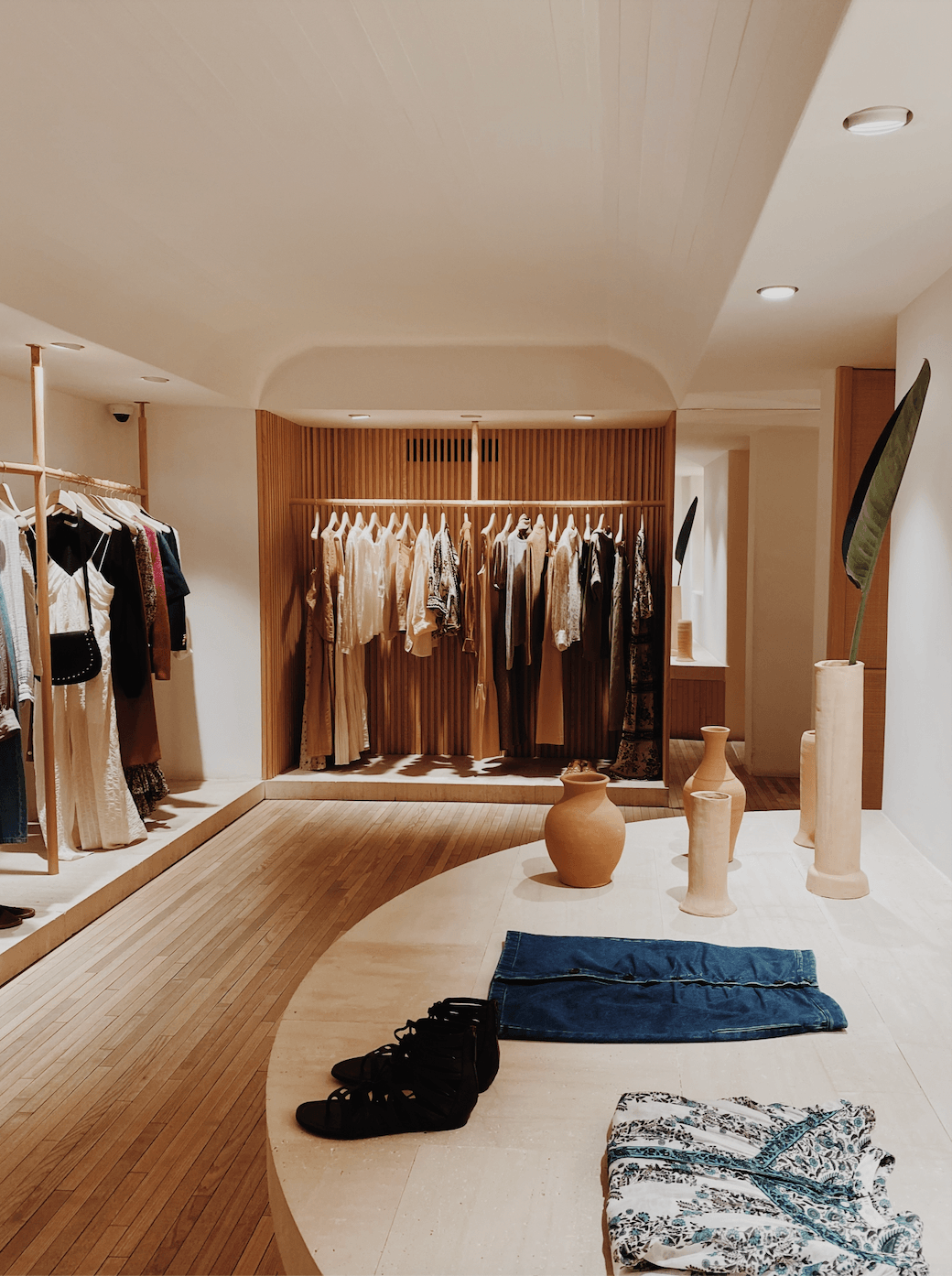MASSCOB, Balearic Islands — Minimalist boutique showroom with wooden display rails, neutral palette, terracotta vessels, and natural light filtering through recessed ceiling fixtures.