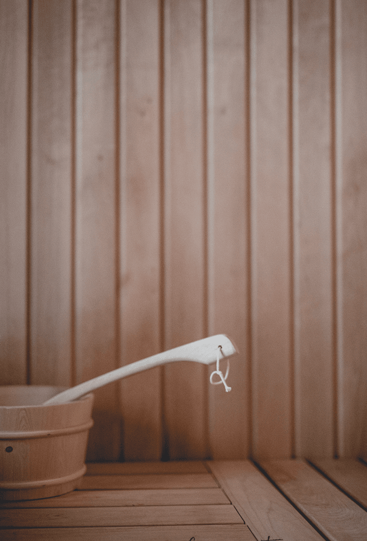 Le Barn Spa, Europe — Wooden sauna interior with vertical paneling, ladle with metal handle, and birch bucket in minimalist Nordic spa setting