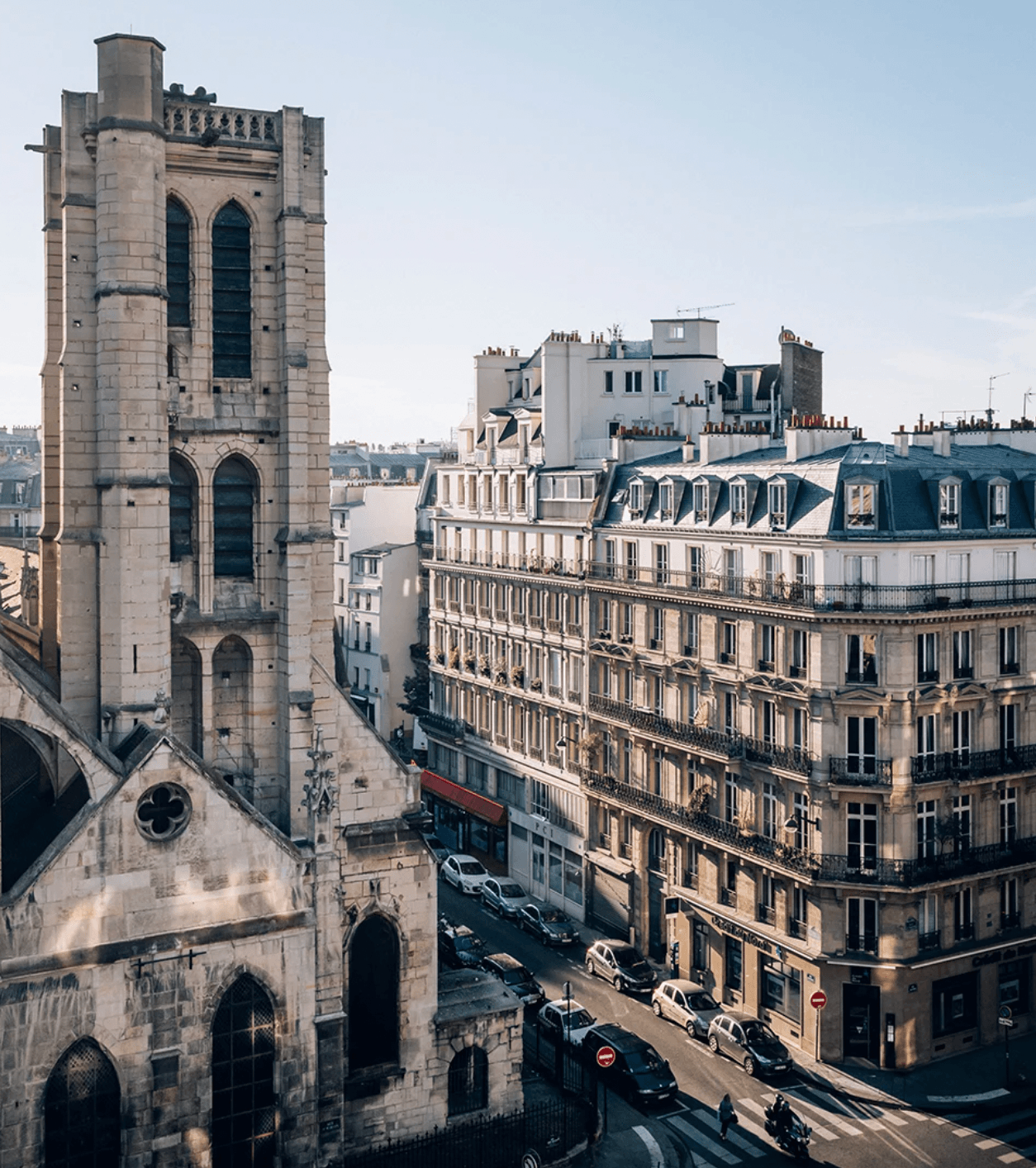 Hôtel National Des Arts, Europe — Stone Gothic tower and Haussmann-style buildings converge on sunlit Parisian street with period architecture and classical facades.