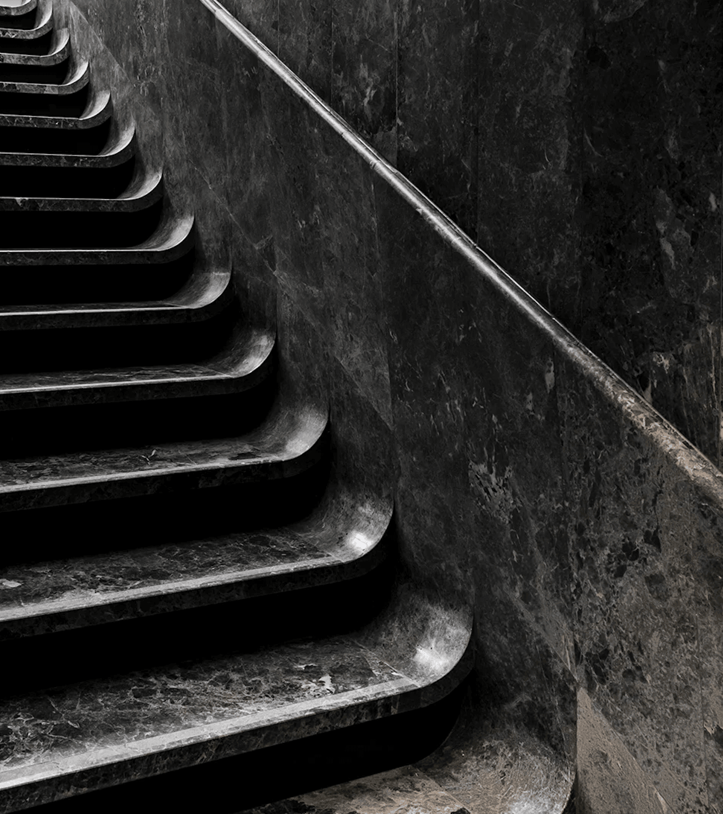 Hôtel National Des Arts, Europe — Dark stone staircase with dramatic side lighting casting sharp shadows on textured walls, minimalist architectural detail.
