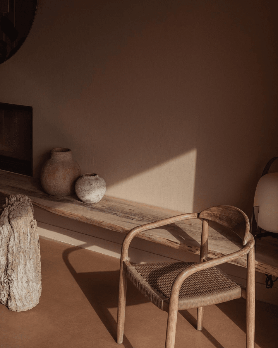Alcúdia House, Balearic Islands — Minimalist interior with wooden chair, textured ceramic vessels, and warm sunlight casting geometric shadows on terracotta wall.