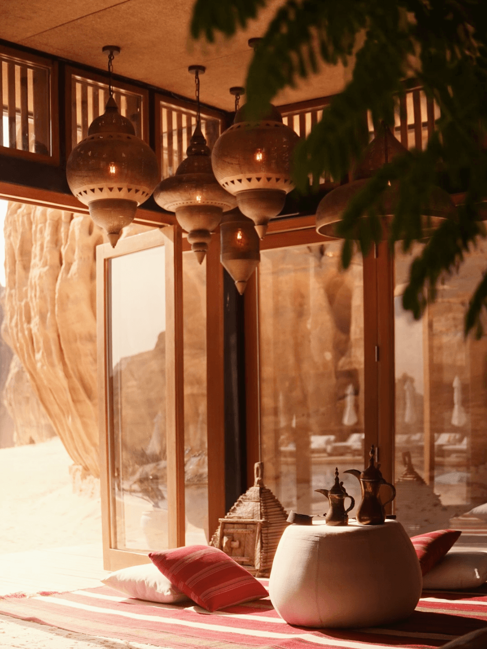 Habitas AlUla — Moroccan-style lounge with perforated brass pendant lights, terracotta walls, cushioned seating, and sheer curtains filtering warm desert light.