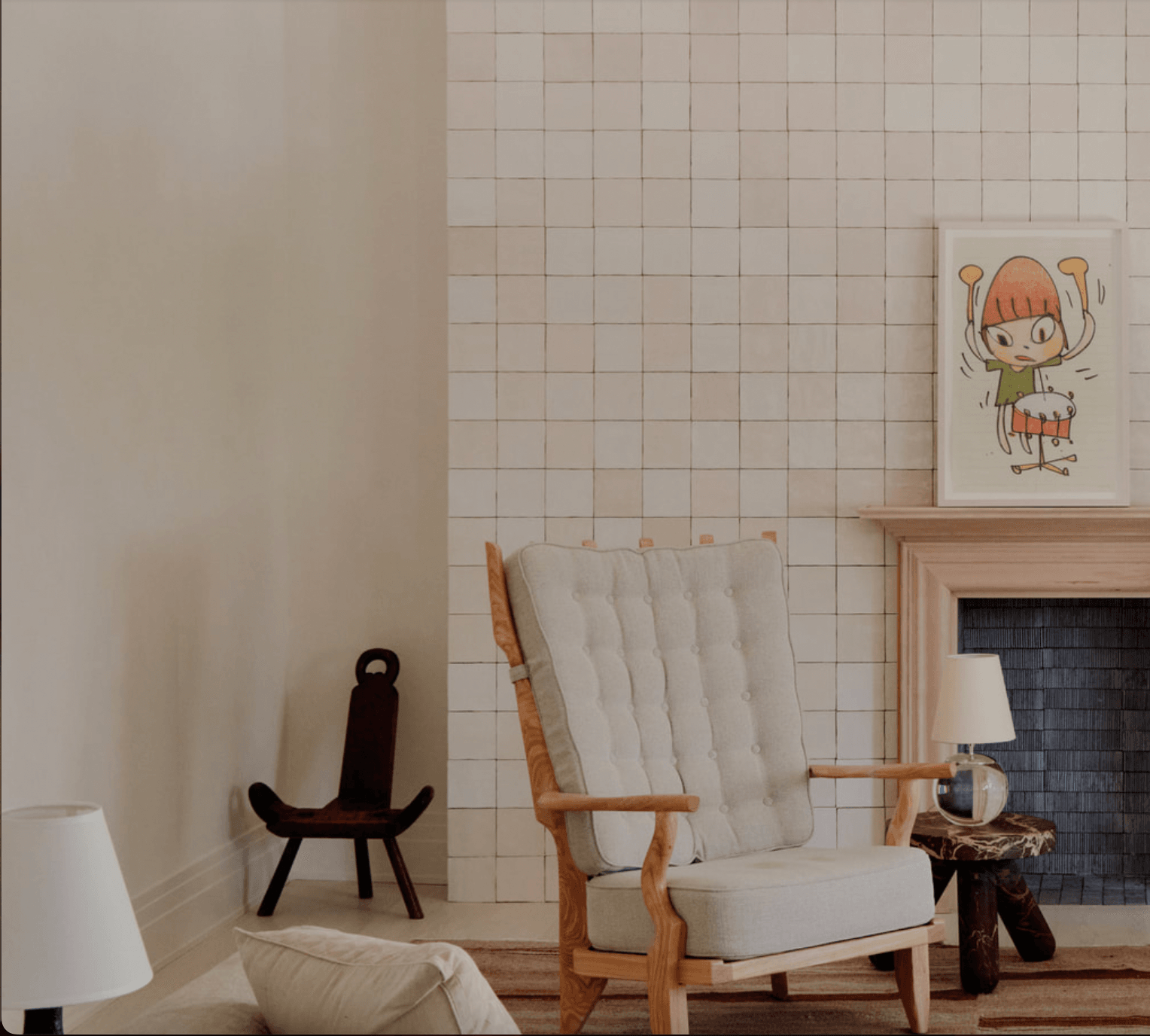 The James Bradley, North America — Mid-century modern living room with cream upholstered chair, sculptural wooden accent seating, grid tile walls, fireplace, and children's artwork.
