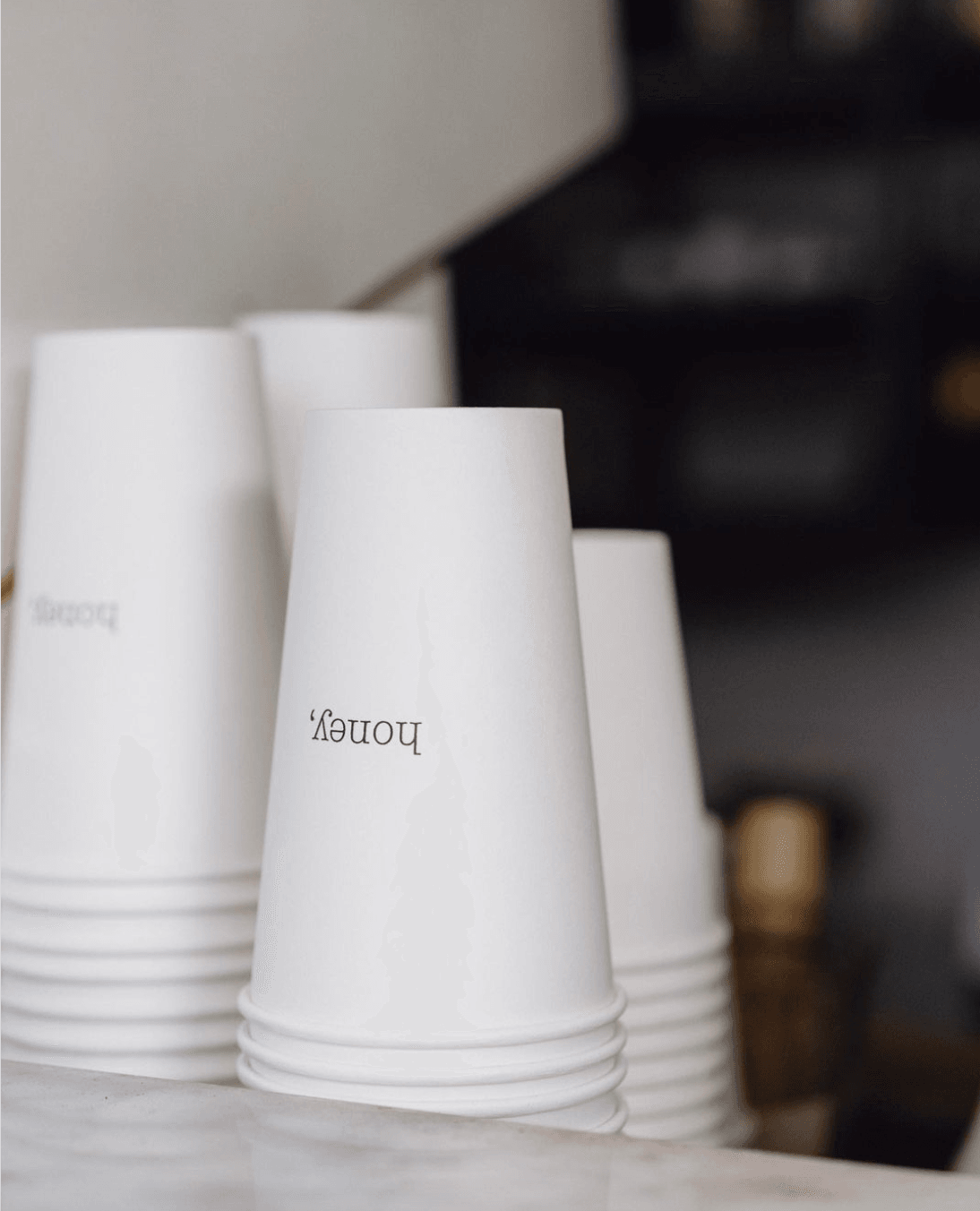 Honey Kitchen, Asia-Pacific — White ceramic cups with branded text arranged on marble surface, minimalist luxury hospitality design with soft natural light.