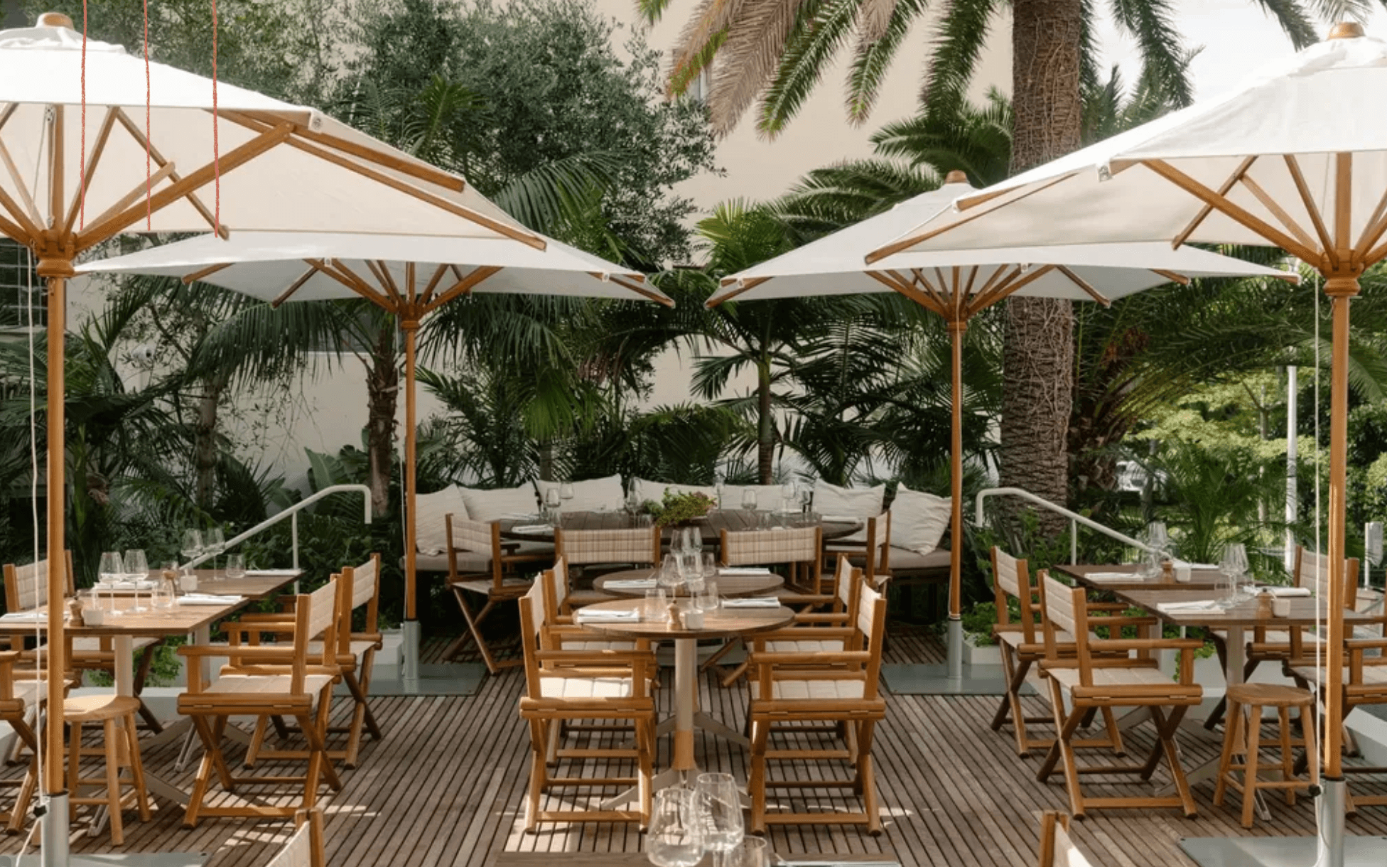 Restaurant Villa, Europe — Shaded dining terrace with wooden umbrellas, natural light, palm trees, teak furniture, and lounge seating amid lush gardens.