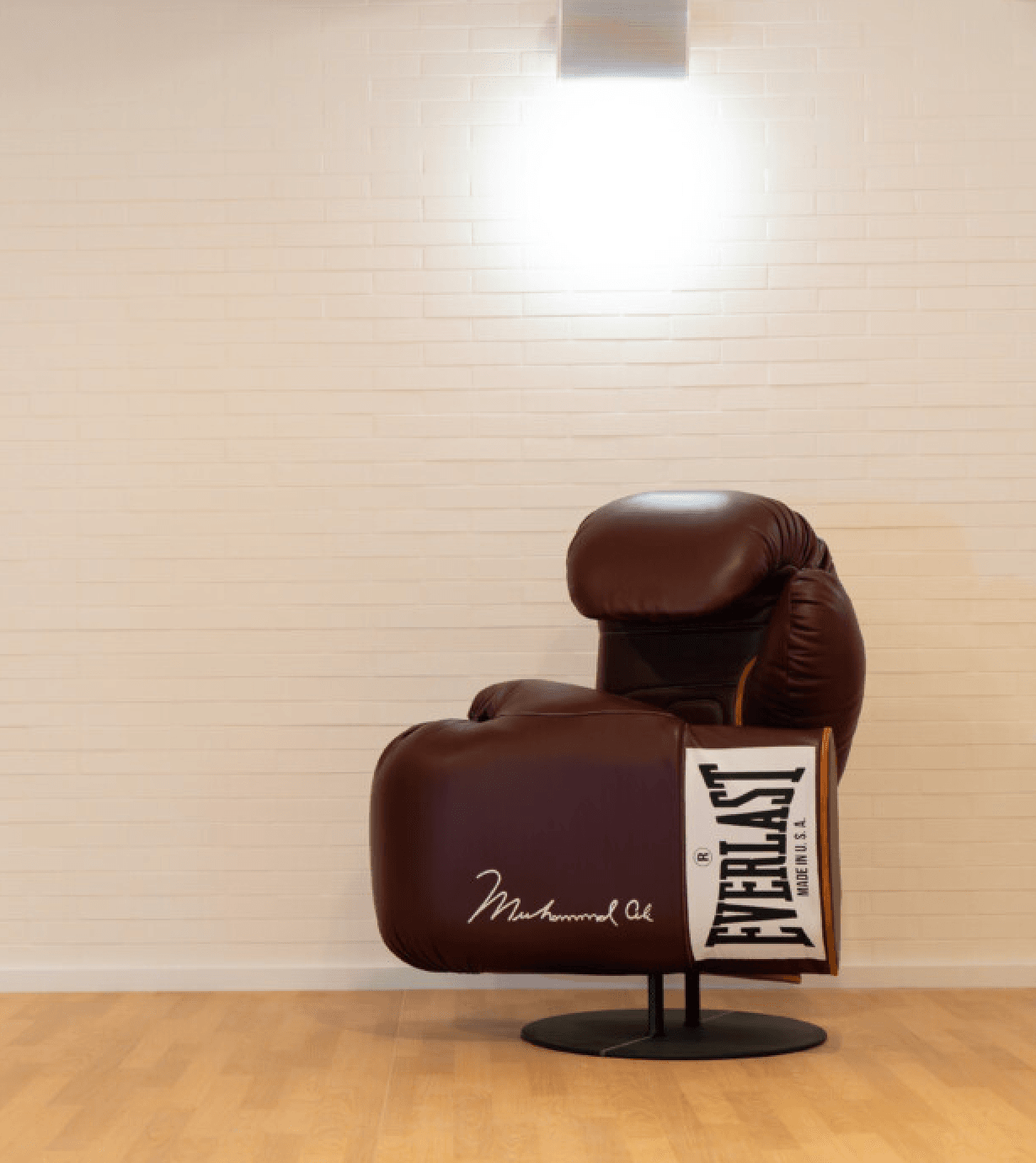 Le C Club, Europe — Dark brown Everlast boxing glove signed by Muhammad Ali, displayed on black stand against cream brick wall with skylight.