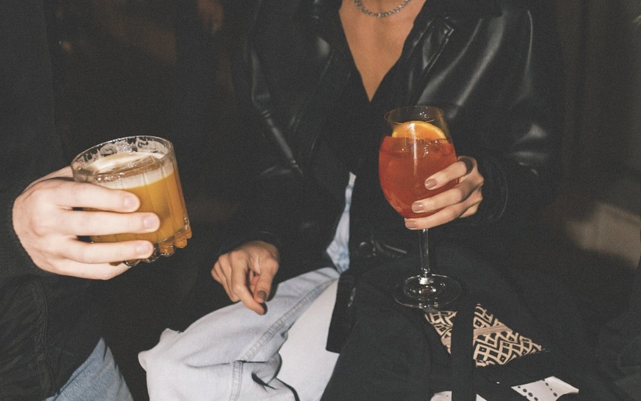 Birdman, Europe — Two people holding cocktails in dark leather jackets at an evening social gathering, ambient low lighting and intimate atmosphere.