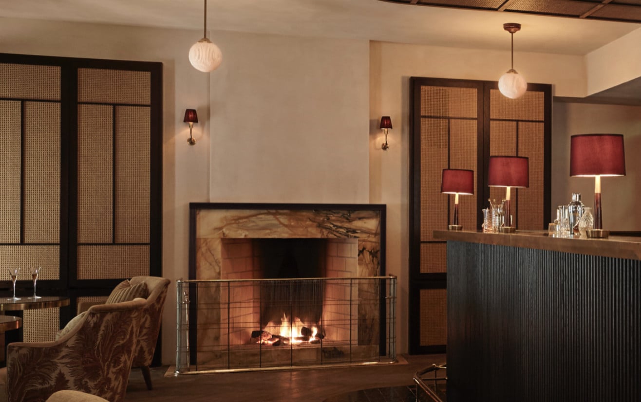 Tata Cocktail Bar, Europe — Mid-century modern lounge with marble fireplace, rattan screen doors, pendant lighting, and leather seating in warm neutral tones.