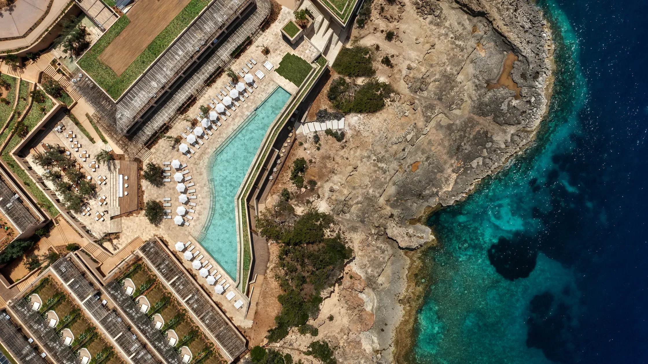 Six Senses Ibiza, Balearic Islands, Spain — Aerial view of clifftop pool overlooking turquoise Mediterranean waters, terraced loungers, limestone geology, modernist architecture.