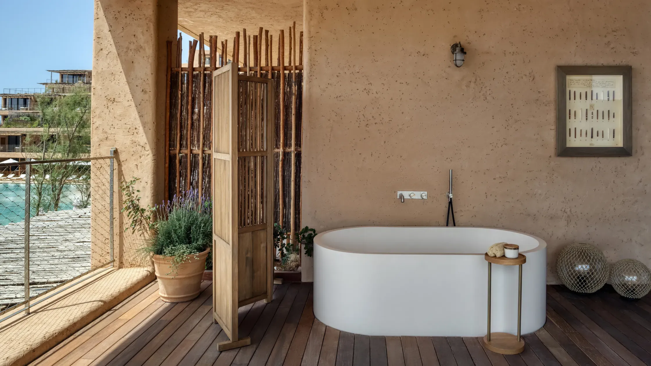Six Senses Ibiza, Balearic Islands, Spain — Outdoor bathroom with white soaking tub, cork walls, wooden deck, and ocean views through glass railing.