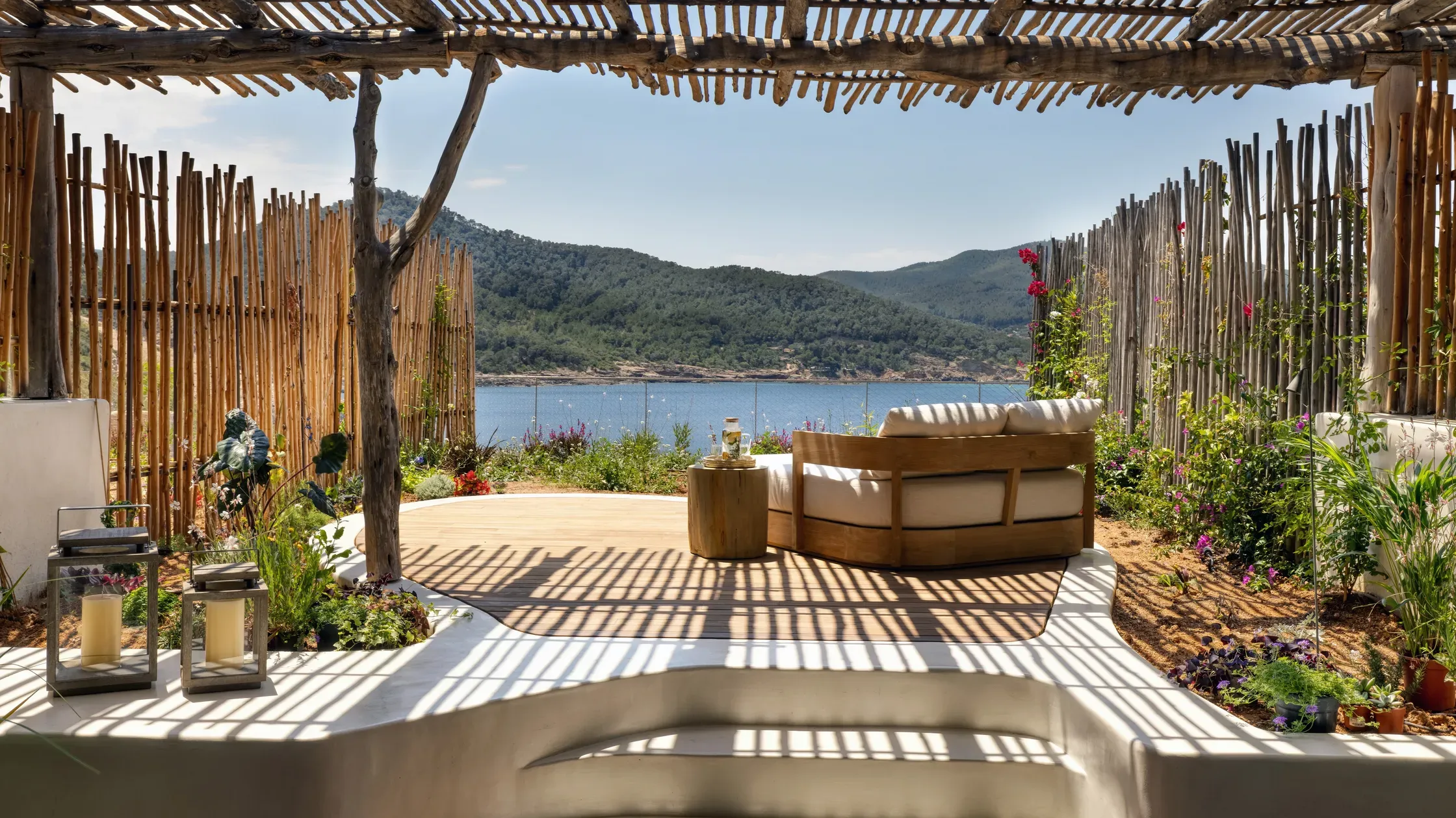 Six Senses Ibiza, Balearic Islands, Spain — Pergola-shaded terrace with curved seating overlooking Mediterranean bay, wooden screens, flowering vines, and forested hills.