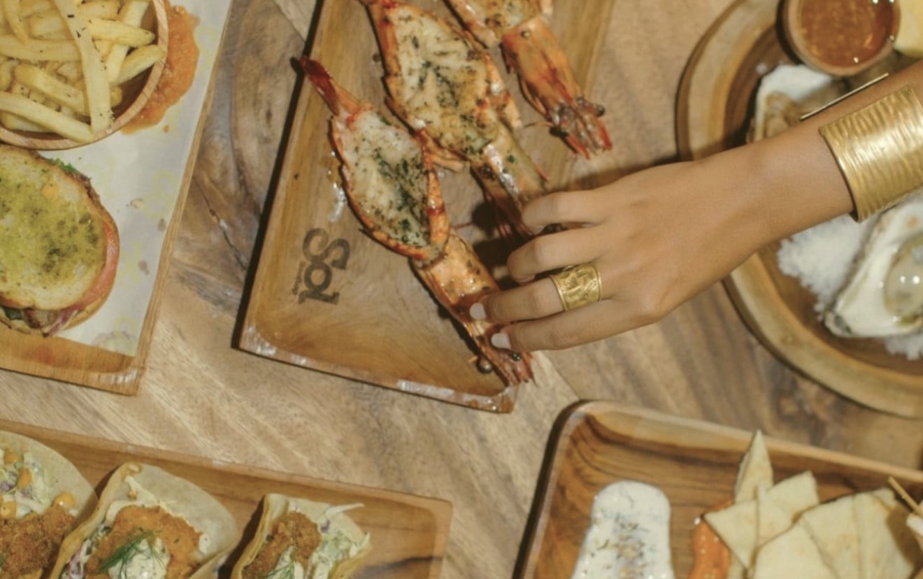 Sol Rooftop Bali, Bali, Indonesia — hand reaching for herb-crusted seafood on wooden serving boards with coastal appetizers and natural light