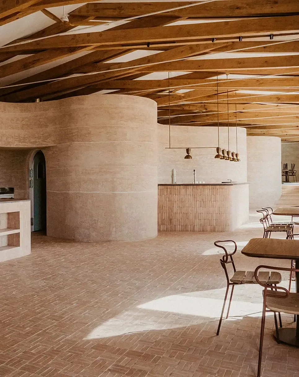 Son Blanc Farmhouse, Balearic Islands, Spain — Rammed earth rotunda with exposed wooden beams, brick herringbone flooring, and pendant brass lighting in minimalist dining space.