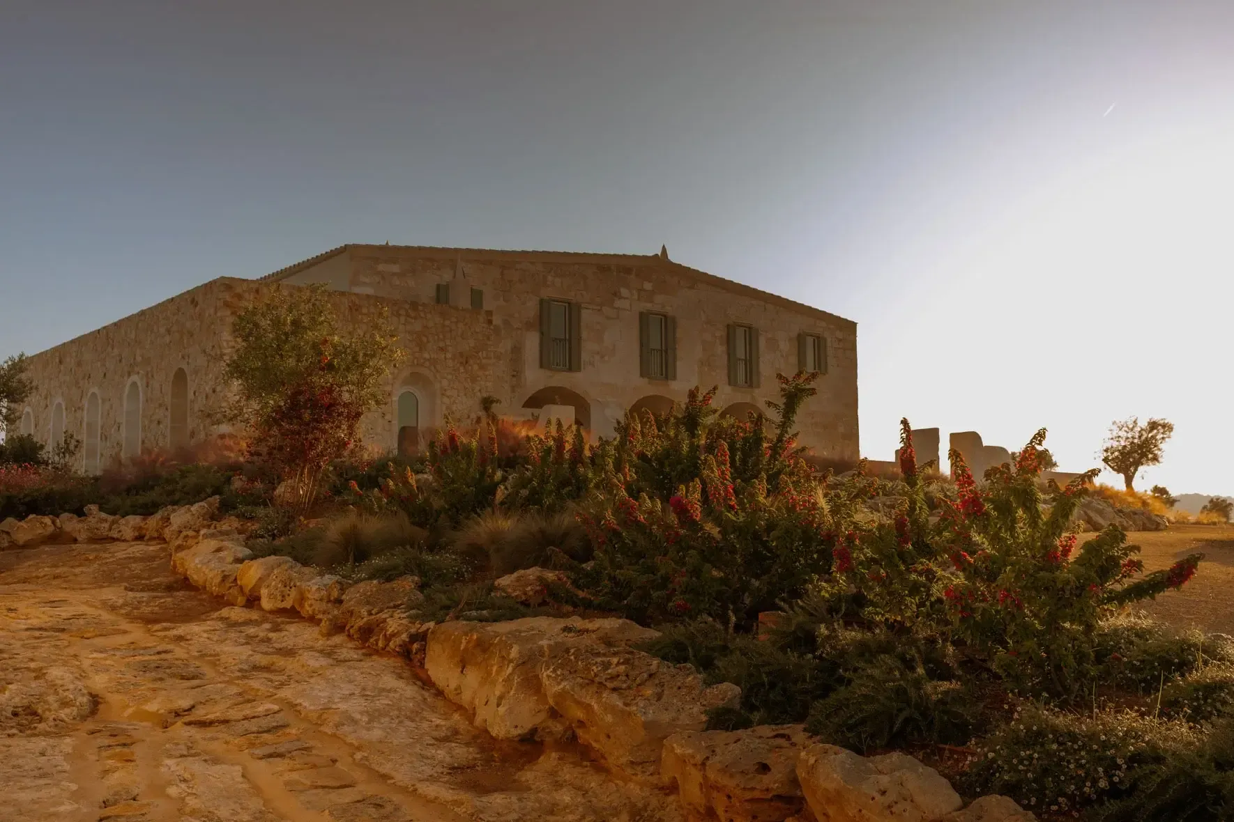 Son Blanc Farmhouse, Balearic Islands, Spain — Ochre stone villa with arched windows overlooking terraced garden and dry landscape at golden hour.