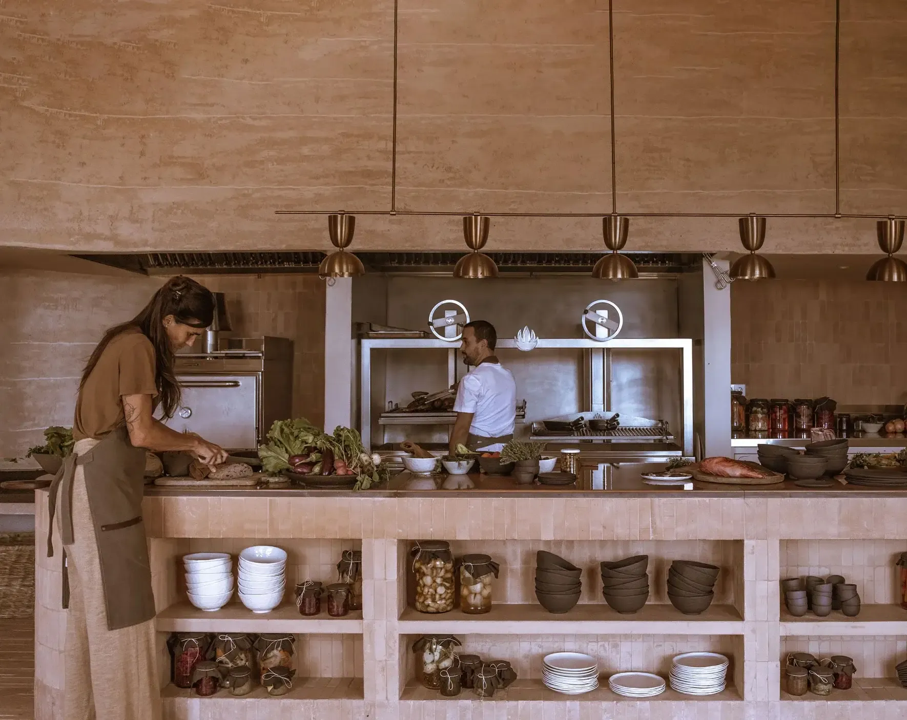 Son Blanc Farmhouse, Balearic Islands, Spain — Open kitchen with terracotta tile counters, brass pendant lights, and shelved ceramics displaying artisanal tableware.