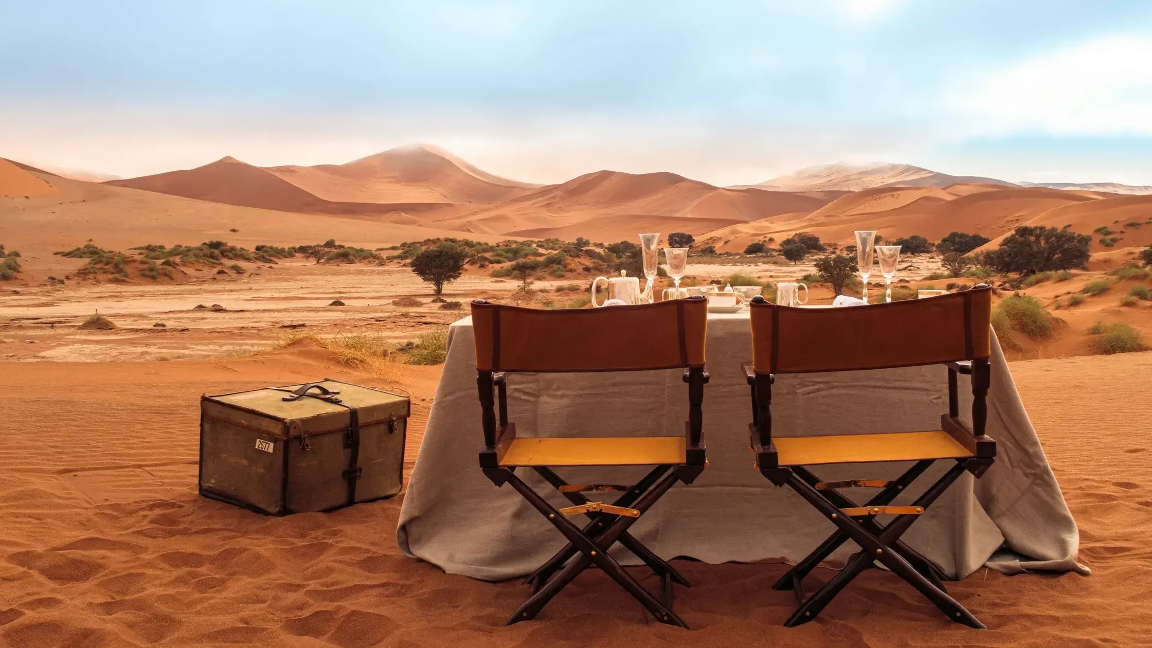 Zannier Sonop, Africa — Desert dining setup with leather directors' chairs, candlelit table, and dune landscape at golden hour.