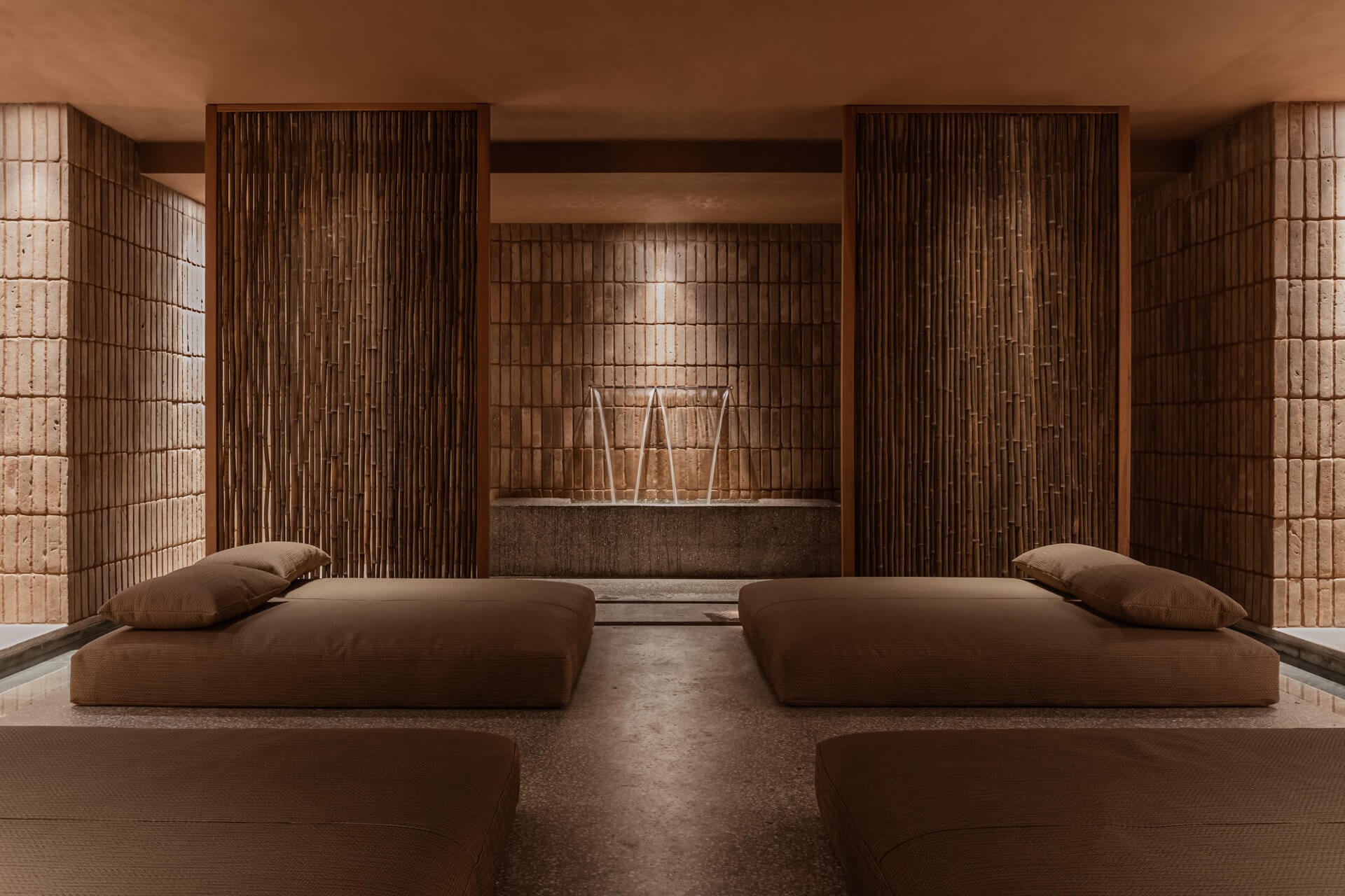 Casa Cook Spa, Europe — Minimalist spa sanctuary with terracotta brick walls, wooden slat screens, concrete platform beds, and warm ambient lighting creating serene wellness retreat.