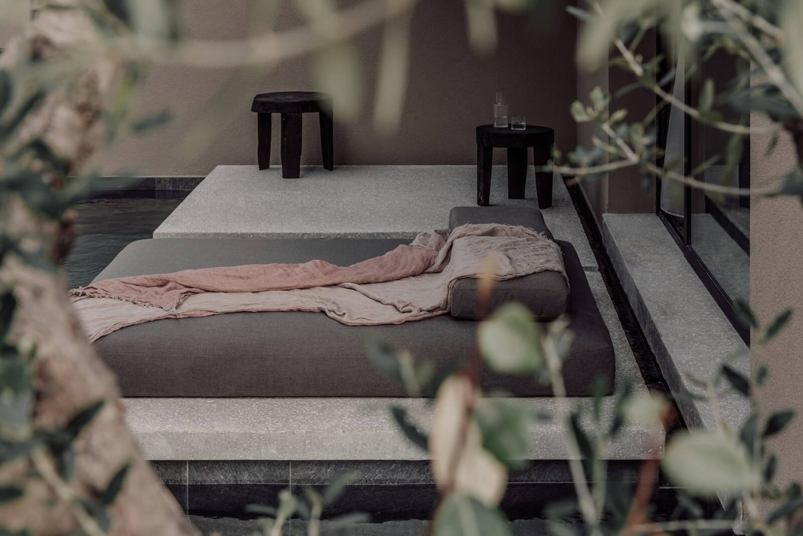 Casa Cook Samos, Greece — Minimalist bedroom with linen bedding, concrete nightstands, black stools, and dried botanicals in soft natural light.