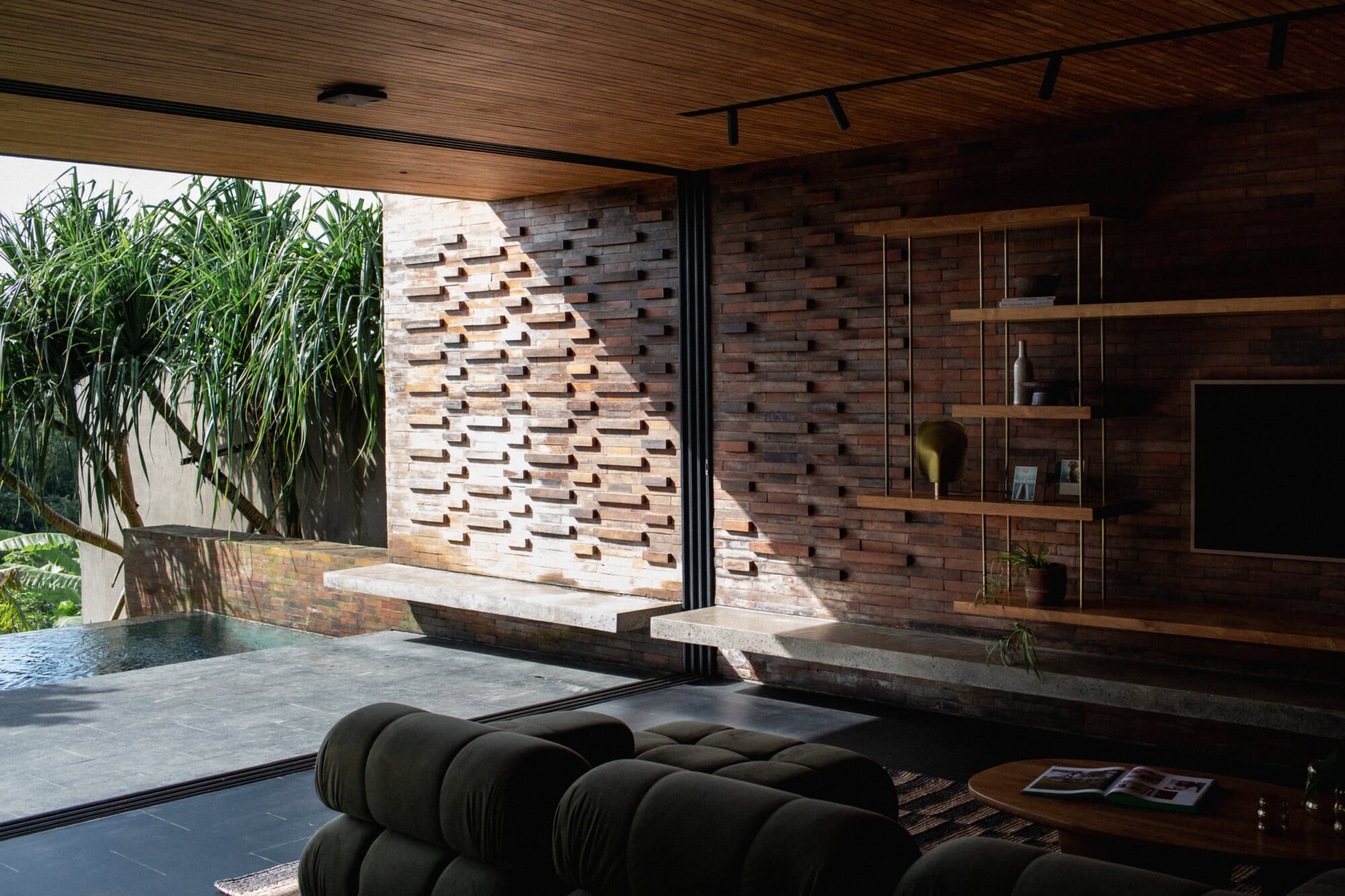 Tegel House, Asia-Pacific — Modern pavilion with brick feature wall, wooden ceiling, black sculptural seating, and floor-to-ceiling glazing opening to landscaped courtyard.