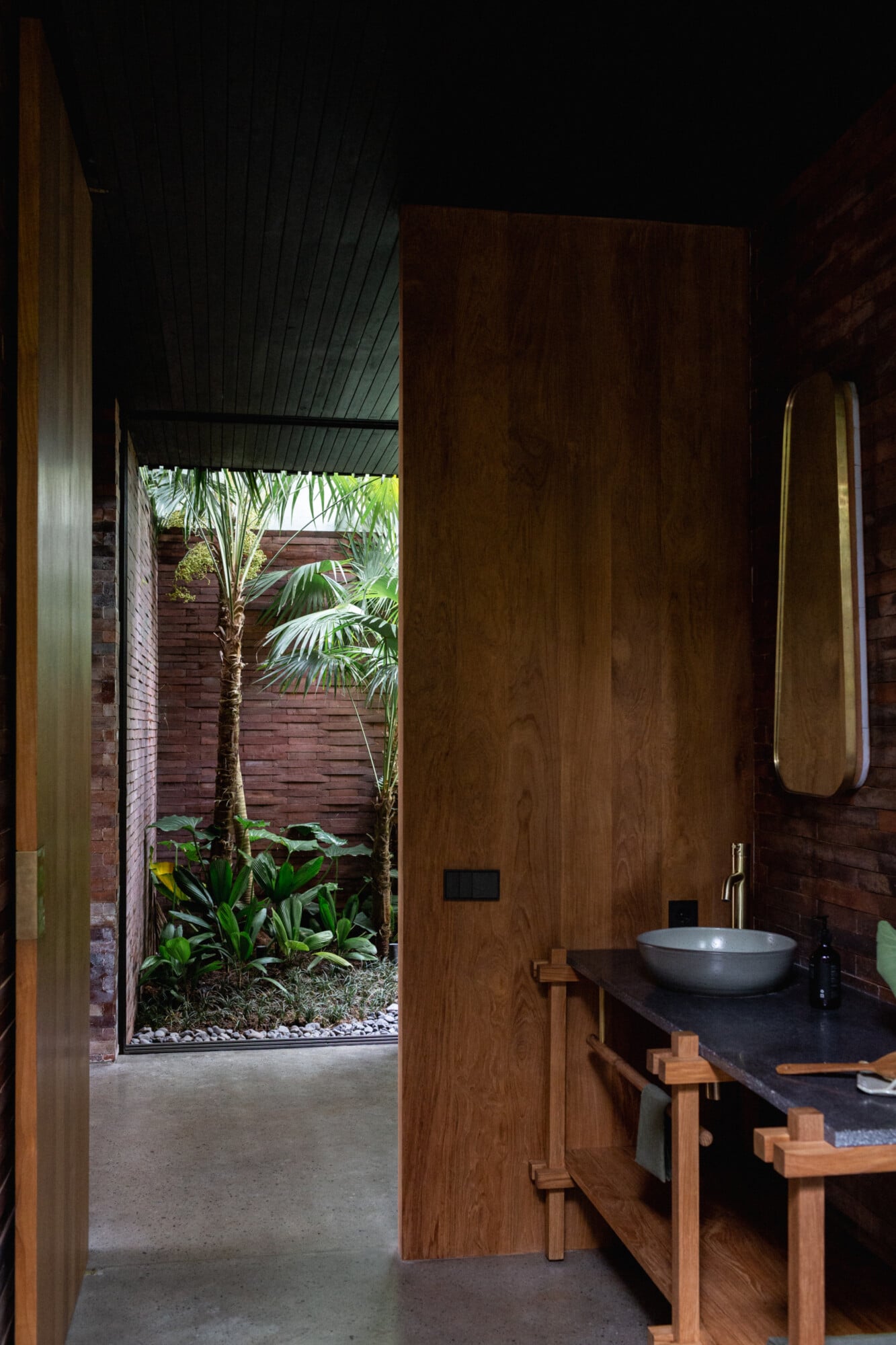 Tegel House, Asia-Pacific — Timber-lined bathroom with stone vessel sink, open courtyard garden view, minimalist wood furnishings, warm natural light.