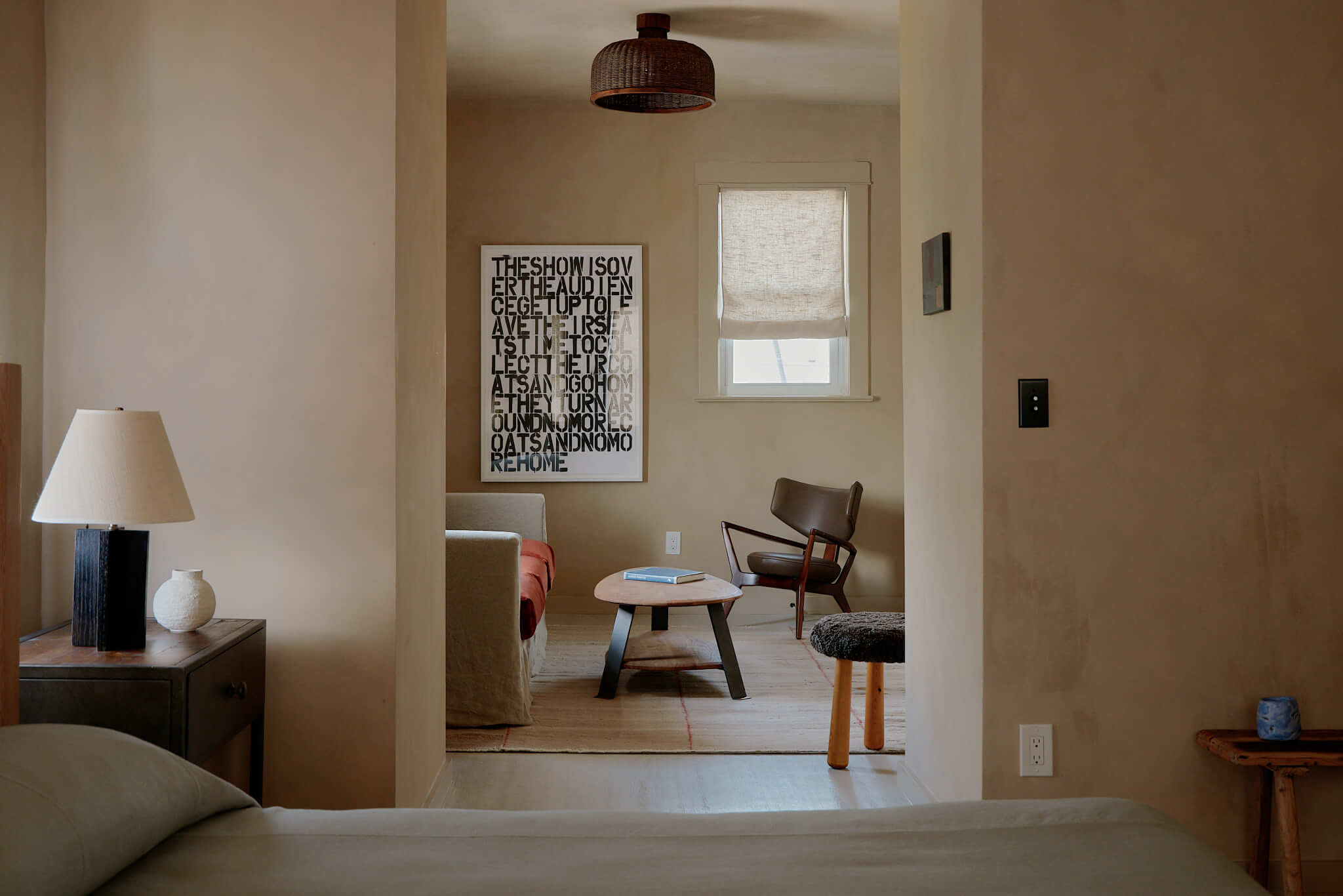 The James Bradley, North America — Minimalist hotel suite with warm beige walls, mid-century modern furniture, natural light, and typographic art.