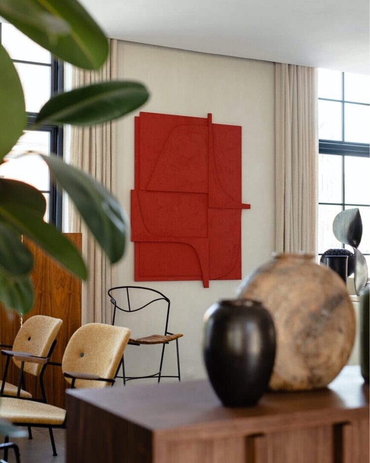 The Audo, Europe — Minimalist hotel lounge with red geometric wall art, natural light, mid-century modern chairs, wooden furniture, potted plant, and sculptural objects.