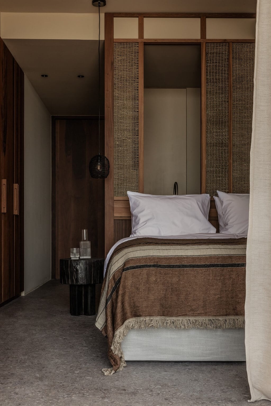 Casa Cook Samos, Greece — Contemporary bedroom with woven wood headboard panels, brown linen bedcover, pendant lamp, and minimalist earthy tones.