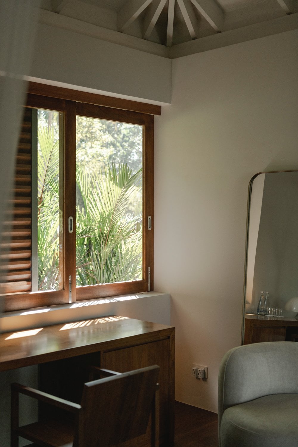Kurulu Bay, Asia — Wooden desk beside sliding glass doors opening to tropical foliage, with angled ceiling detail and natural light flooding minimalist bedroom interior.