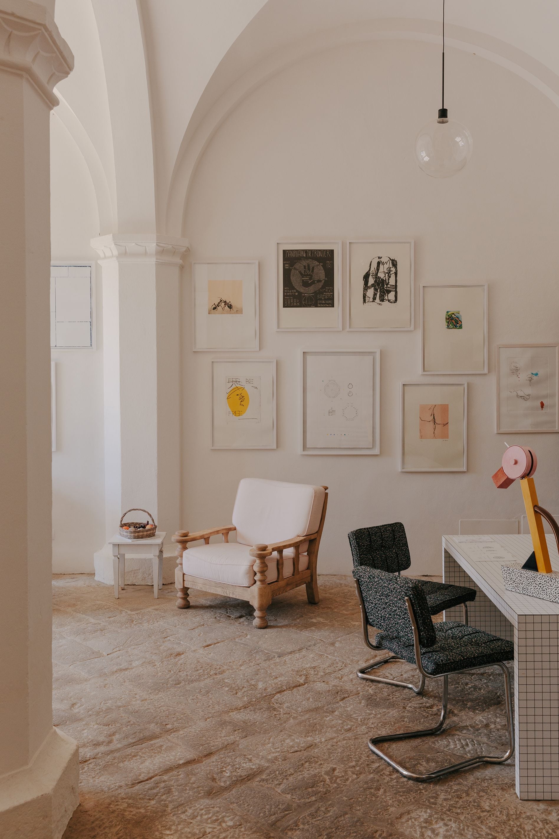 Villa Lena, Europe — Minimalist studio space with arched ceilings, framed artworks, natural light, wooden chair, and modernist furniture on terrazzo flooring.