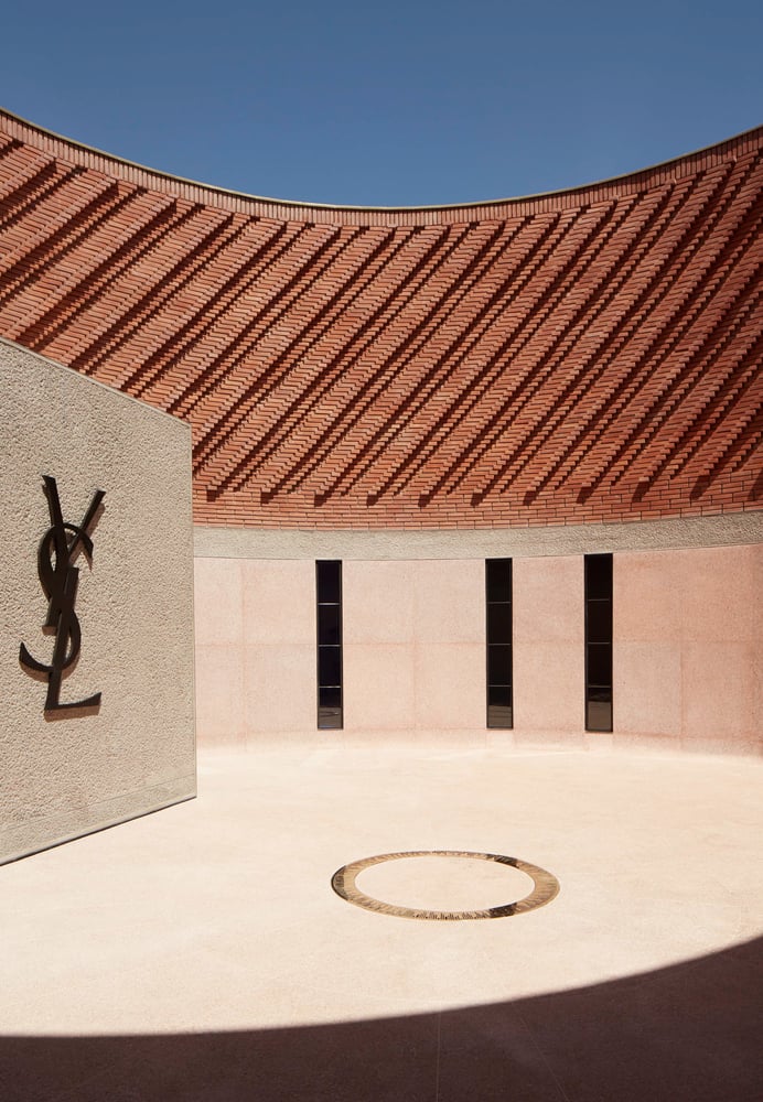Musée YSL Marrakech, Morocco — Curved brick arcade casting geometric shadows over minimalist courtyard with YSL monogram and circular water feature.